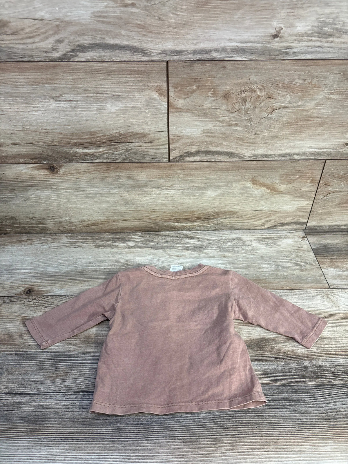 Front view of Cotton On brown baby long sleeve shirt, size 0-3 months, with crew neckline on wood-look floor