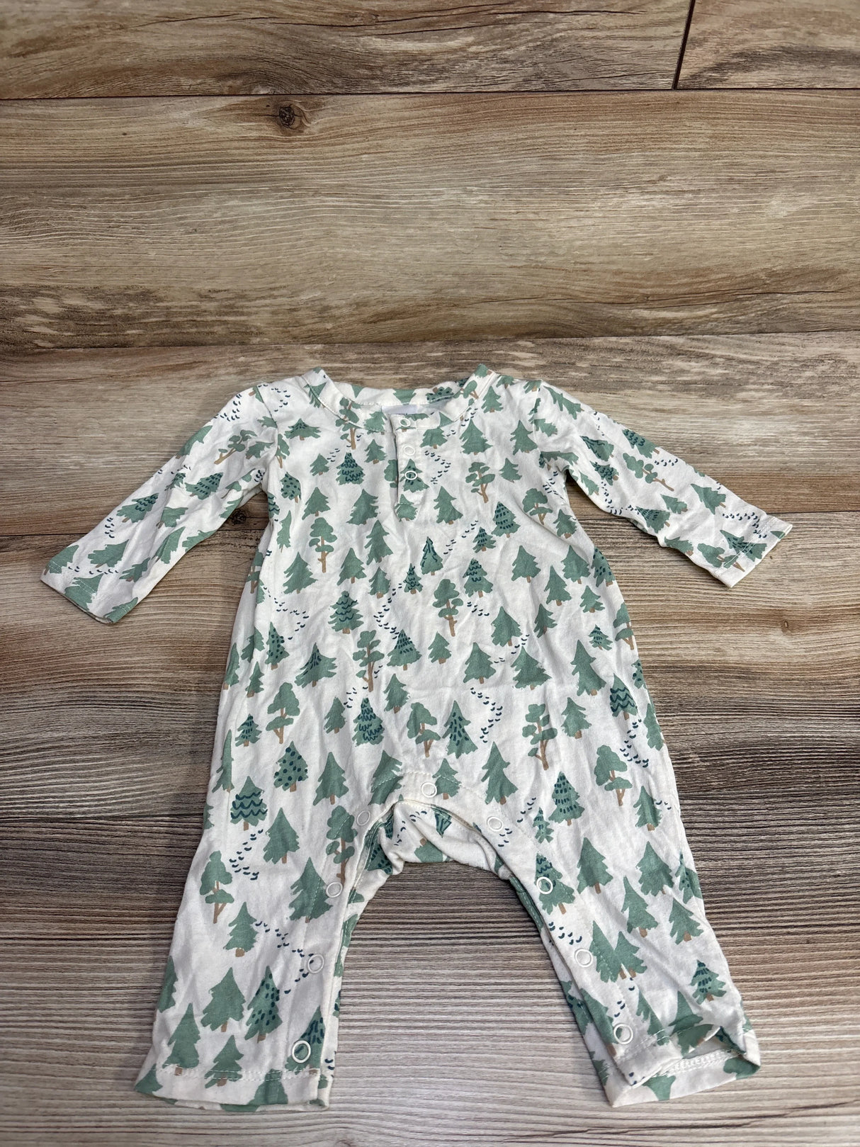 White baby romper with green tree pattern and snap closures, laid on wooden surface