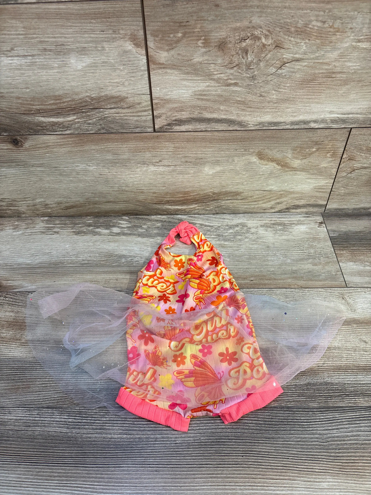 Front view of Ken & Co Girl Power Tulle Overlay Romper in pink showcasing a sheer tulle overlay on a wood-look floor