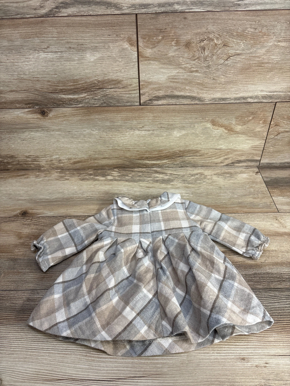 Neutral plaid long-sleeve baby dress with gathered skirt on wood floor background