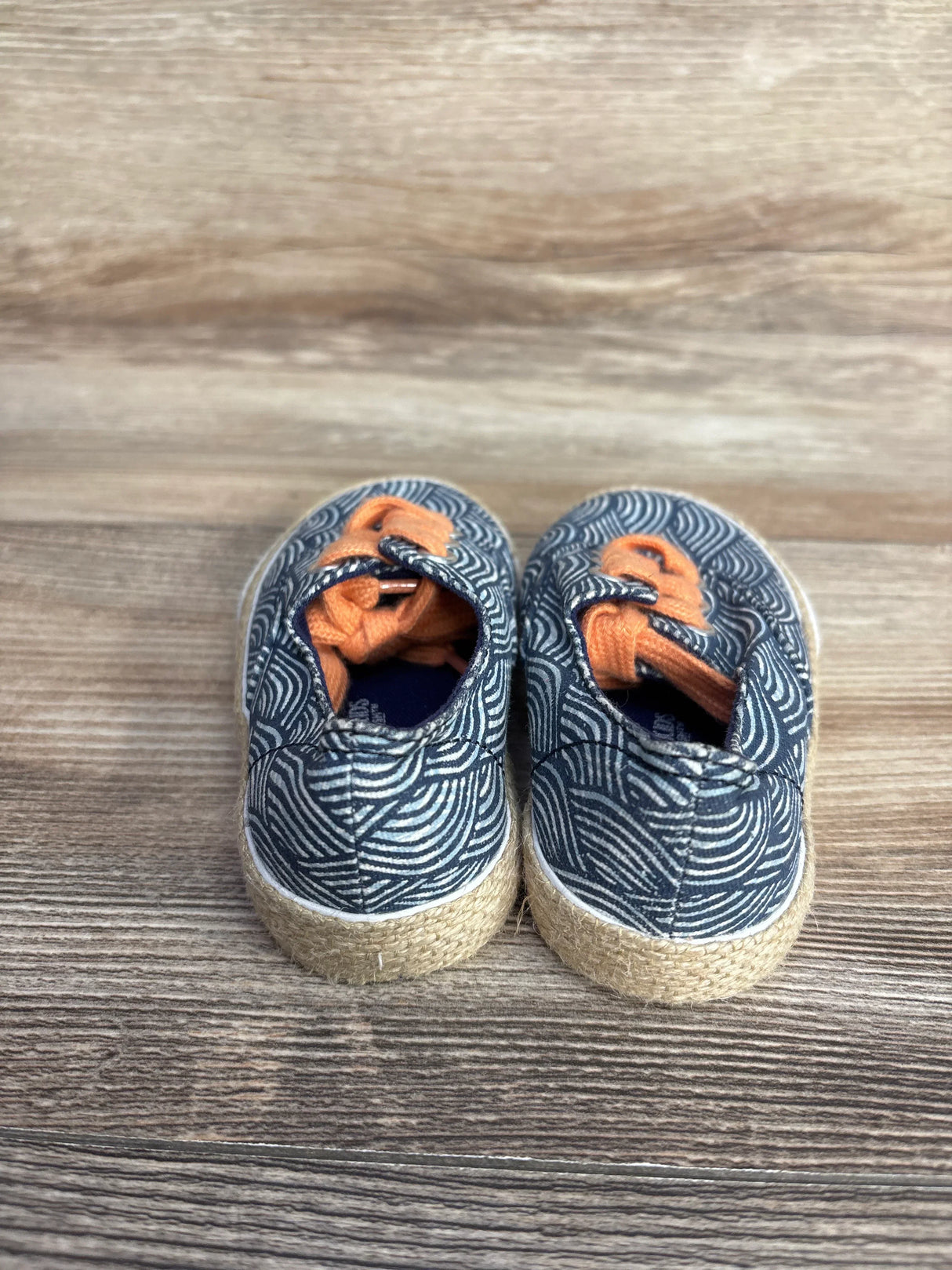 Back view of Genuine Kids from Oshkosh Tailynn Sneakers in blue size 6c showcasing navy wave print canvas orange laces and jute trimmed sole on wood plank floor