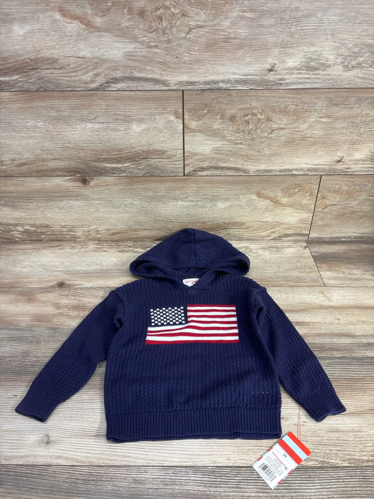 Front flat lay of navy Cat and Jack toddler hooded sweater showing knit American flag on chest on wood plank background