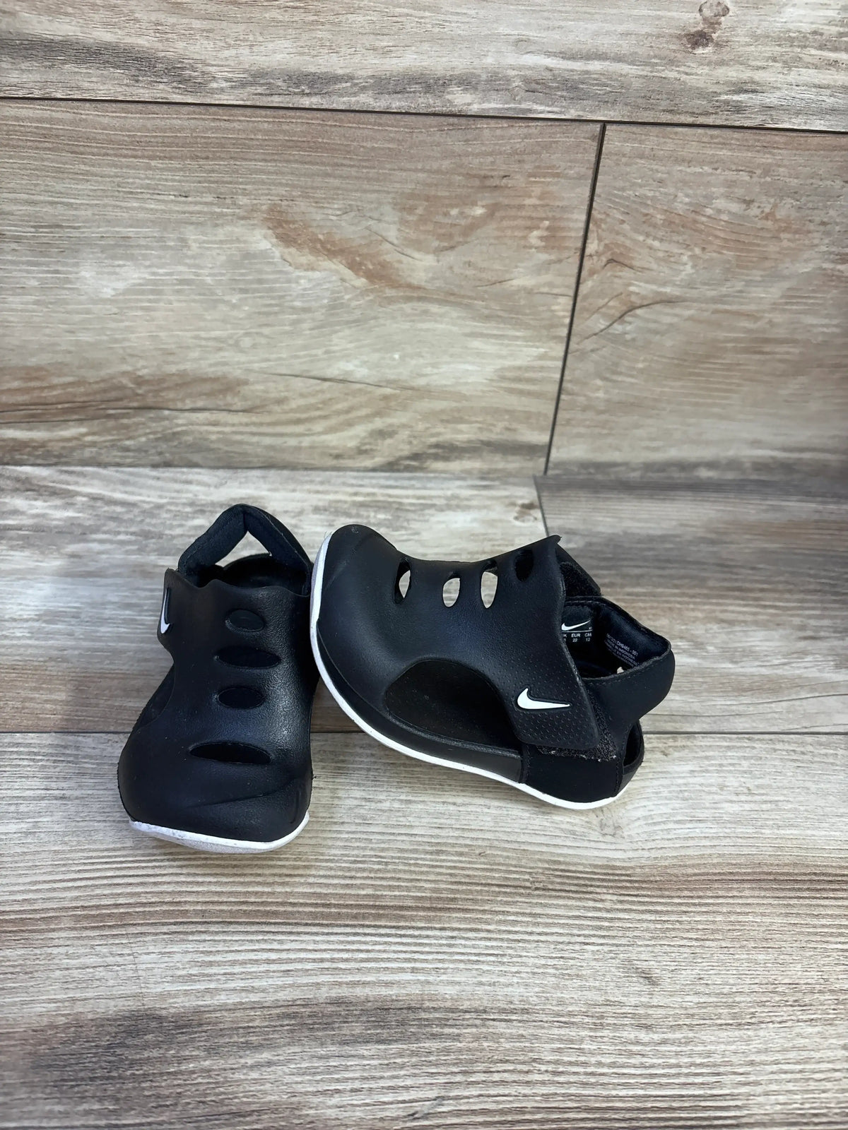 Three-quarter view of Nike Sunray Protect 3 toddler sandals in black with white sole, vented upper and heel strap on wood floor