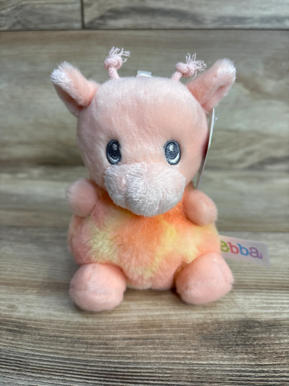 Plush pink and yellow giraffe stuffed animal toy with embroidered eyes on wood background