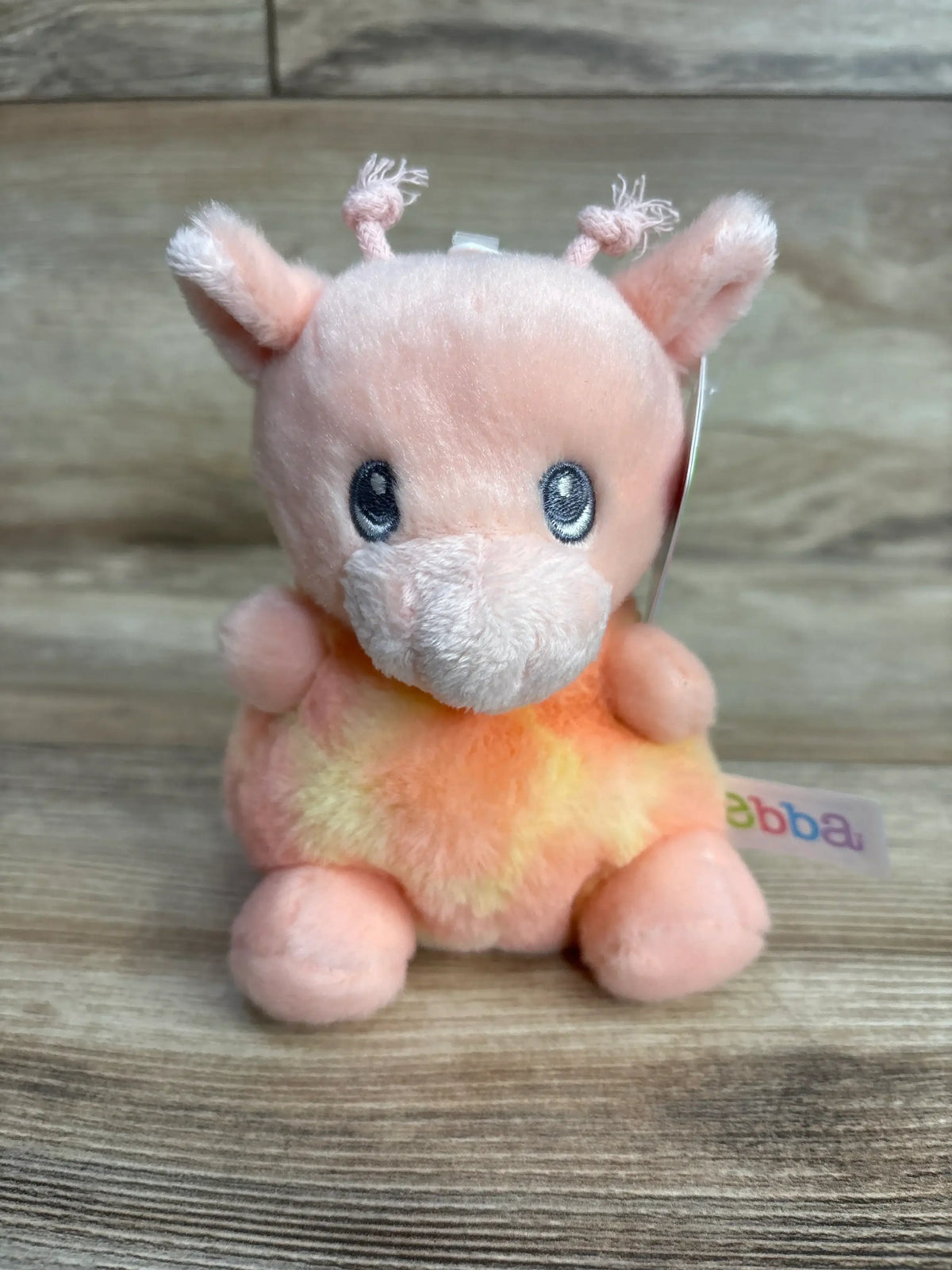Plush pink and yellow giraffe stuffed animal toy with embroidered eyes on wood background