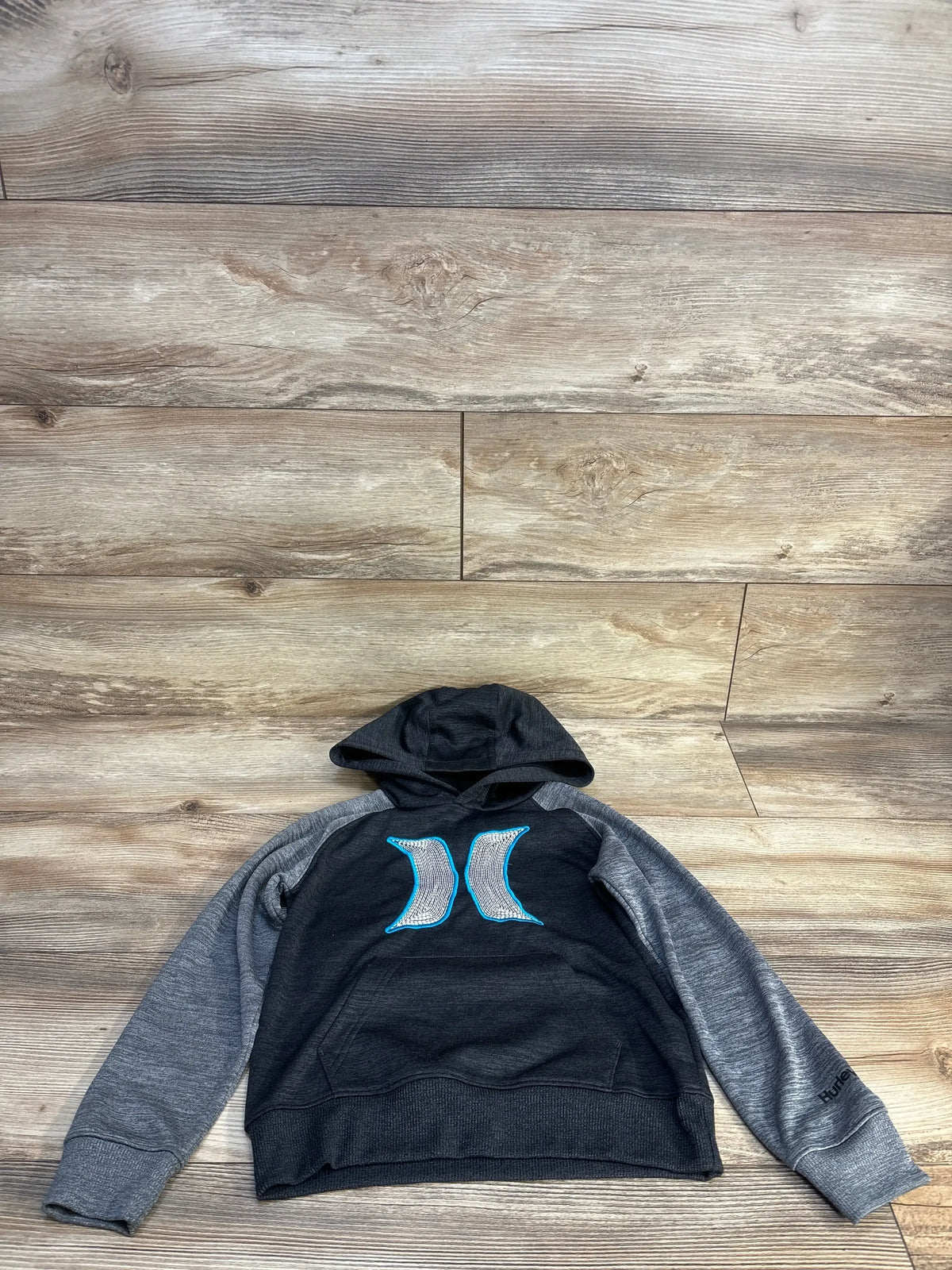 Flat lay of boys Hurley pullover hooded sweatshirt size 5T showcasing blue Hurley logo and gray raglan sleeves on wood floor