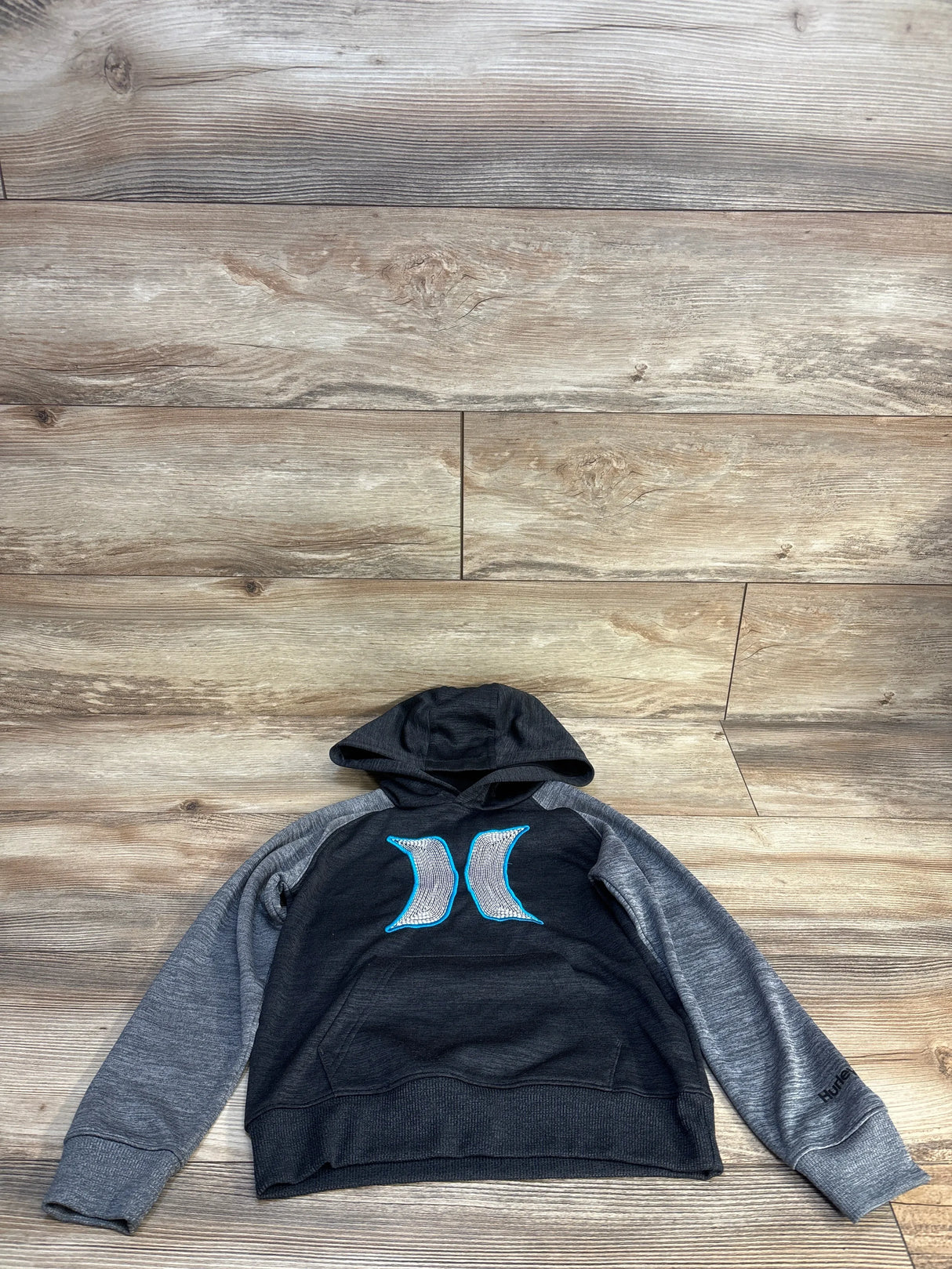 Flat lay of Hurley boys pullover hoodie size 5T, charcoal body with gray raglan sleeves and blue Hurley logo centered on chest on wooden floor