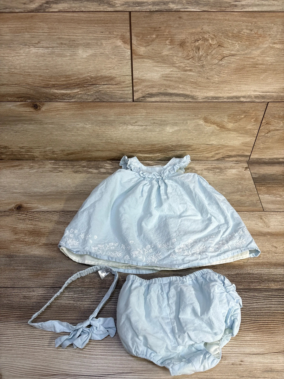 Top view of Joie blue three-piece sleeveless dress set with embroidered dress, bloomers, and headband on a wood floor