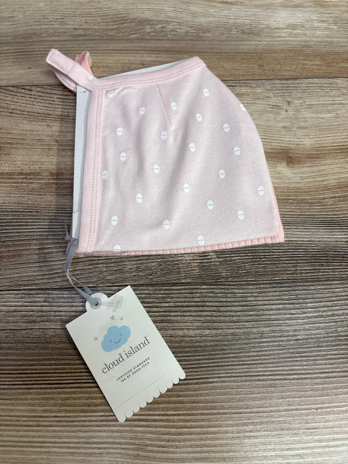 Pink baby hat with white polka dots and Cloud Island tag on wood surface
