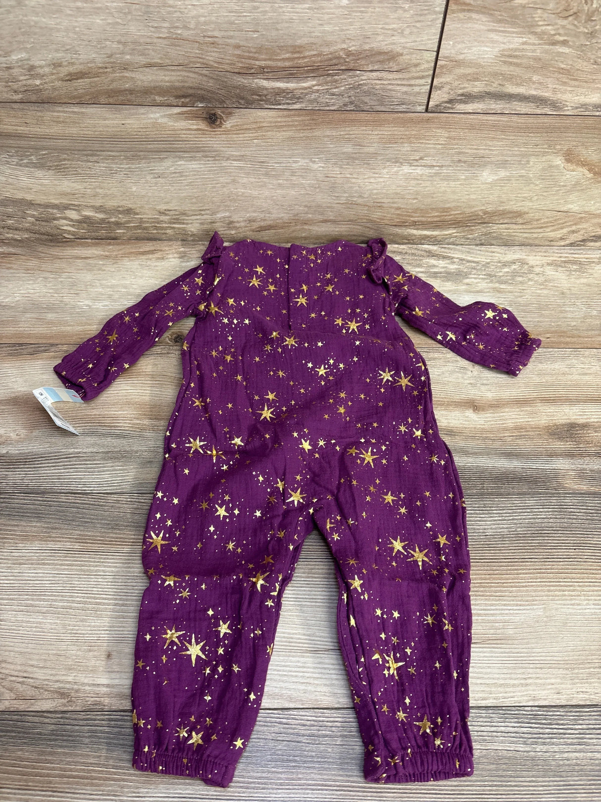 Purple long-sleeve baby romper with gold star print on wooden floor, kids clothing