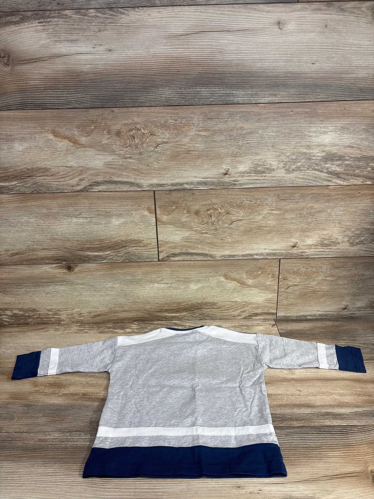 Back view of gray, white, and navy blue long-sleeve toddler shirt on wooden floor background