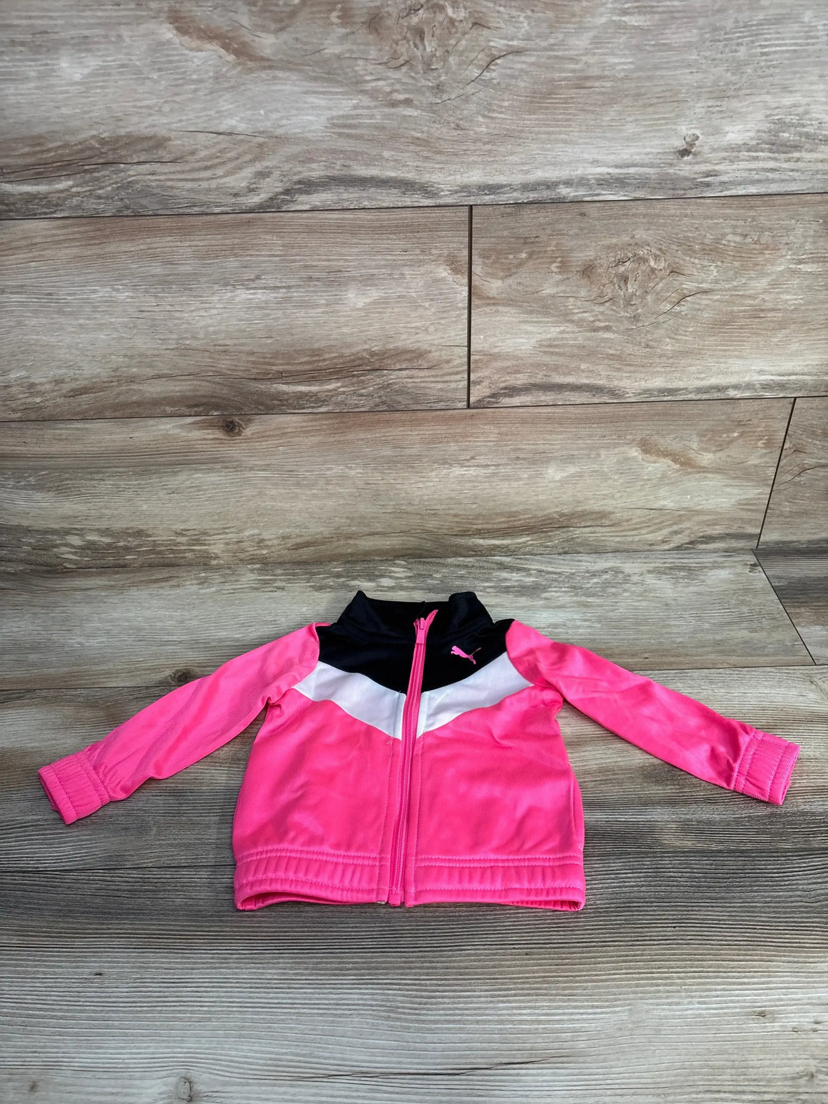 Pink, white, and black Puma toddler jacket with zipper laid flat on wooden floor
