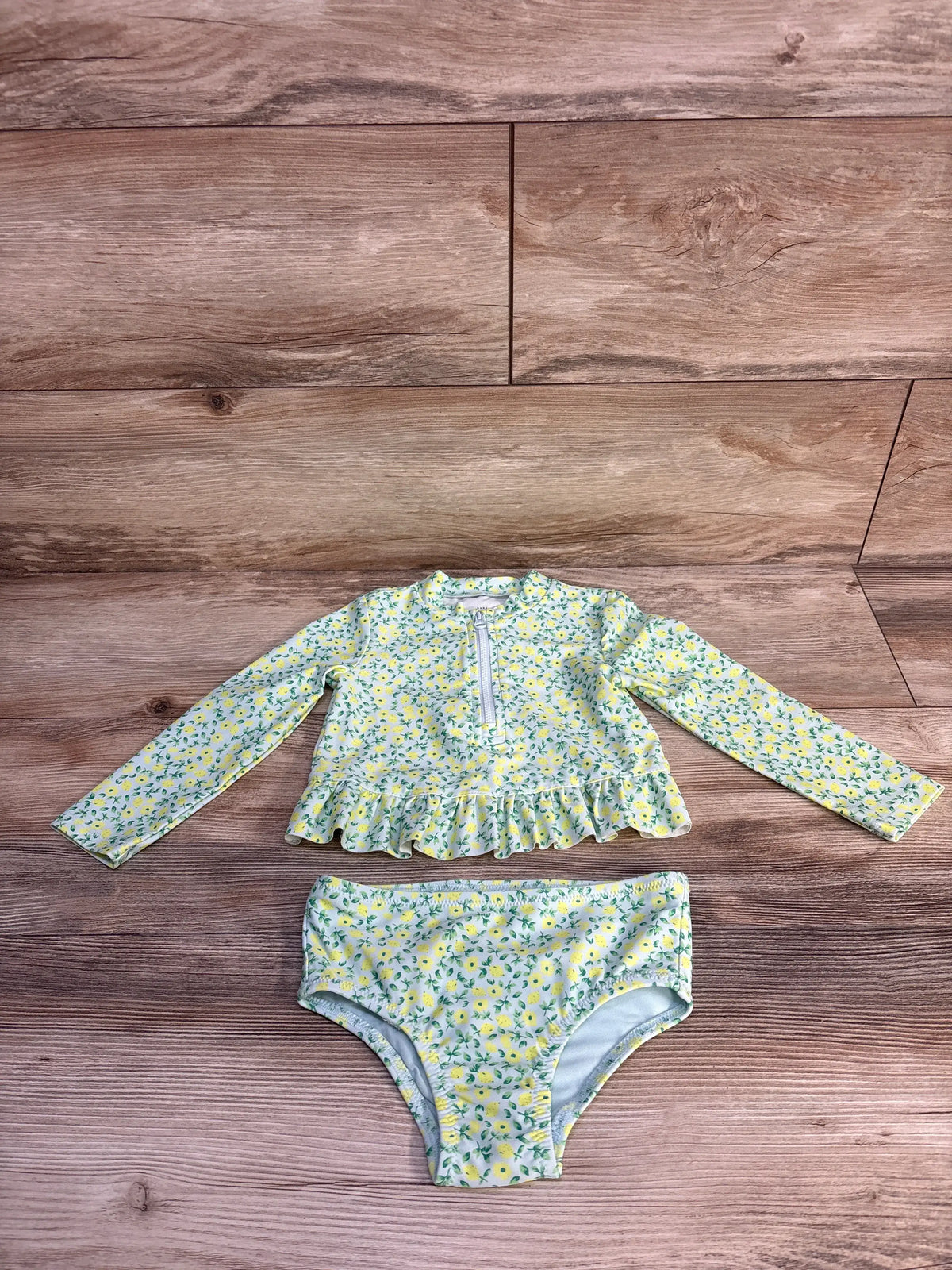 Flat lay of Baby Gap 2-piece rash guard set with zip-front ruffle long-sleeve top and matching teal lemon-print bikini bottoms on wood