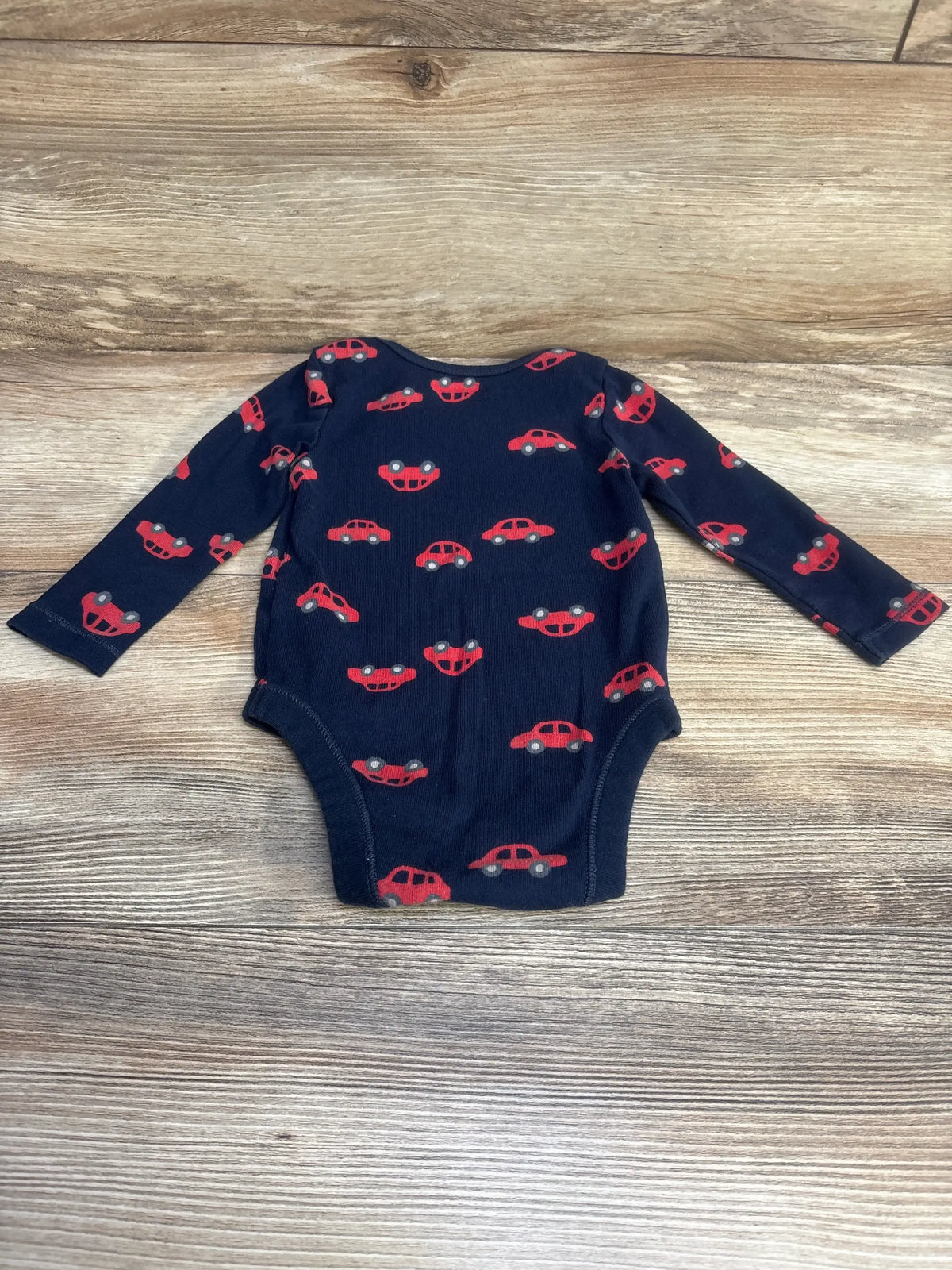 Front view of navy Old Navy long-sleeve baby bodysuit showcasing red car print, laid flat on wood background