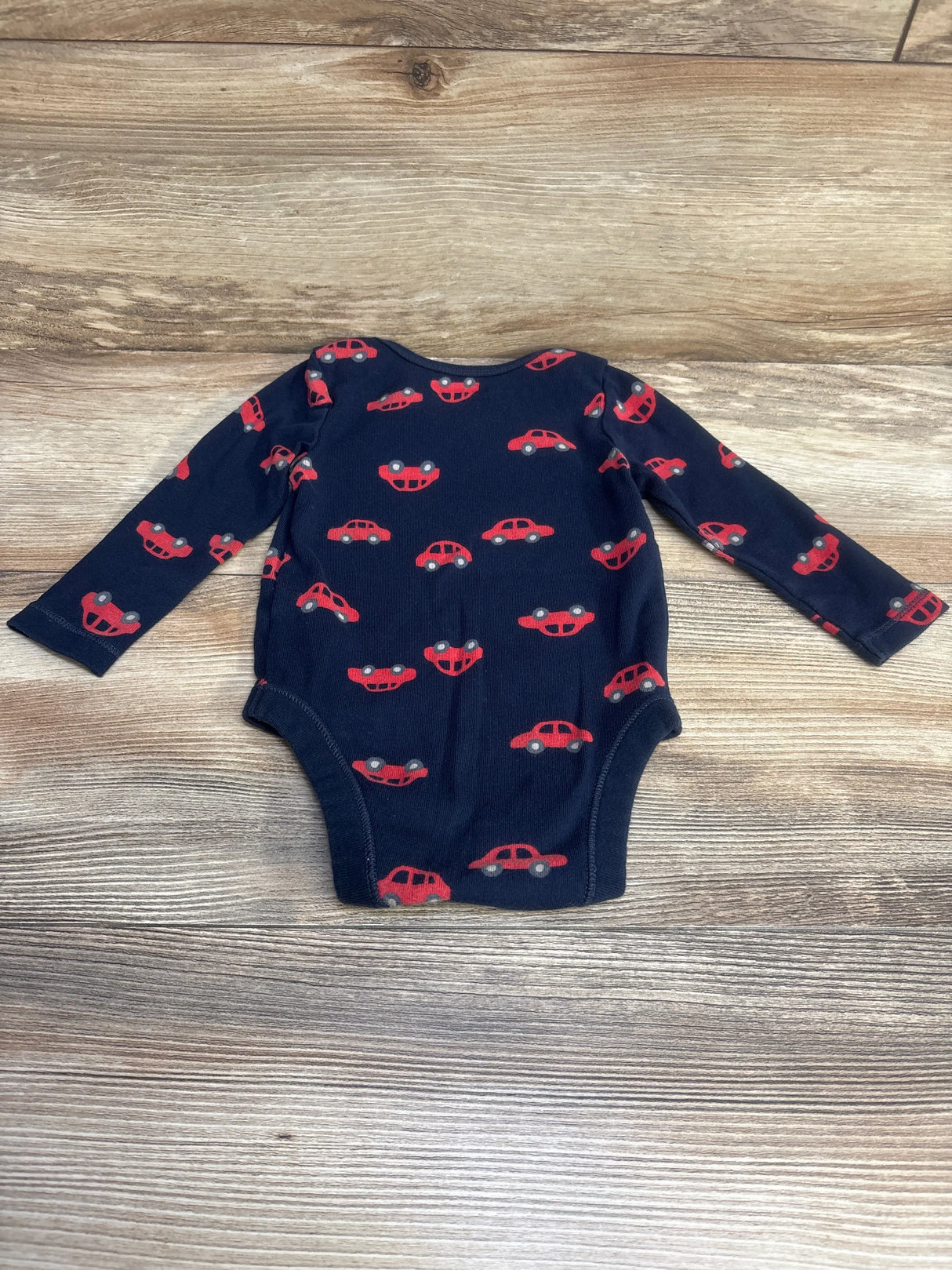 Front view of navy Old Navy long-sleeve baby bodysuit showcasing red car print, laid flat on wood background