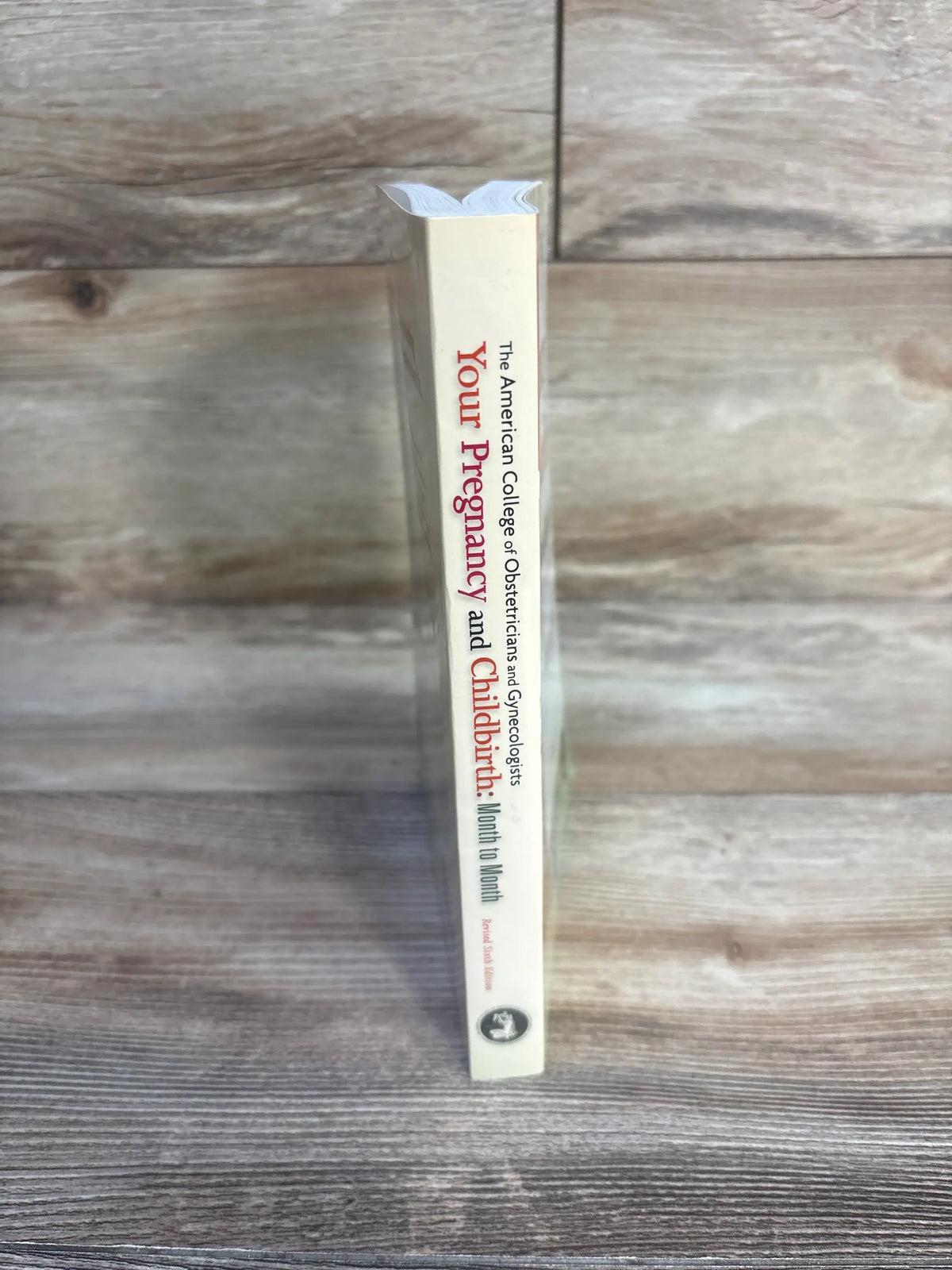 Side view of Your Pregnancy and Childbirth Month to Month Sixth Edition paperback showing title on spine against wood grain
