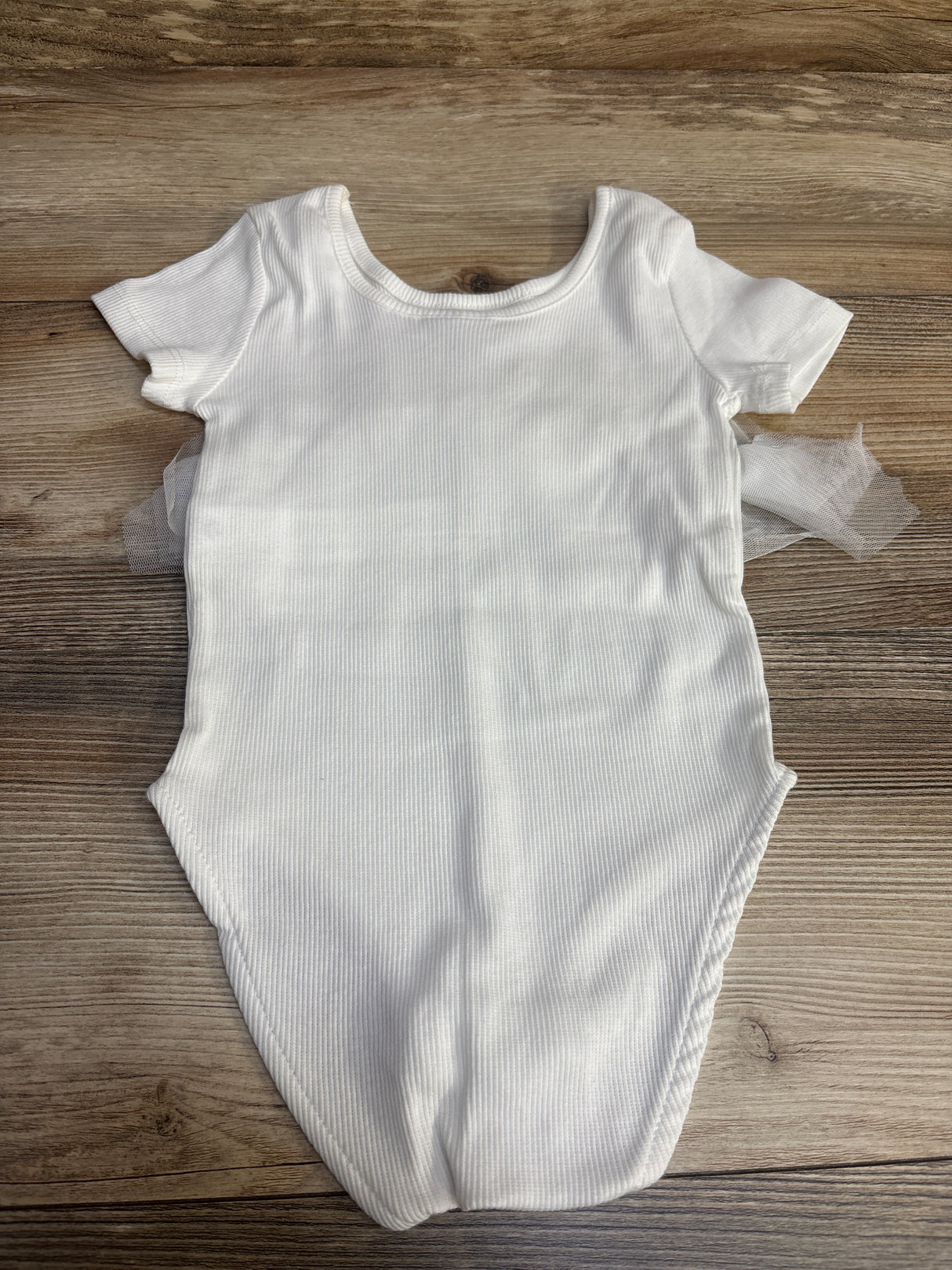 White ribbed baby bodysuit with short sleeves on wood background
