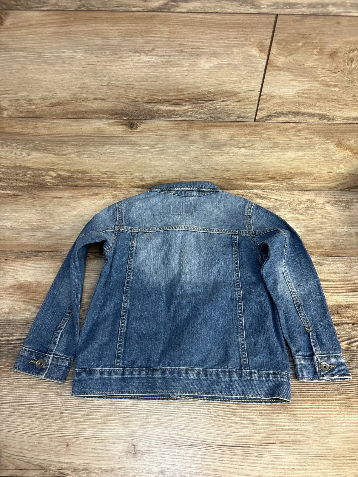 Back view of blue Children’s Place denim jacket size 5T showing faded wash and seam details on wood floor