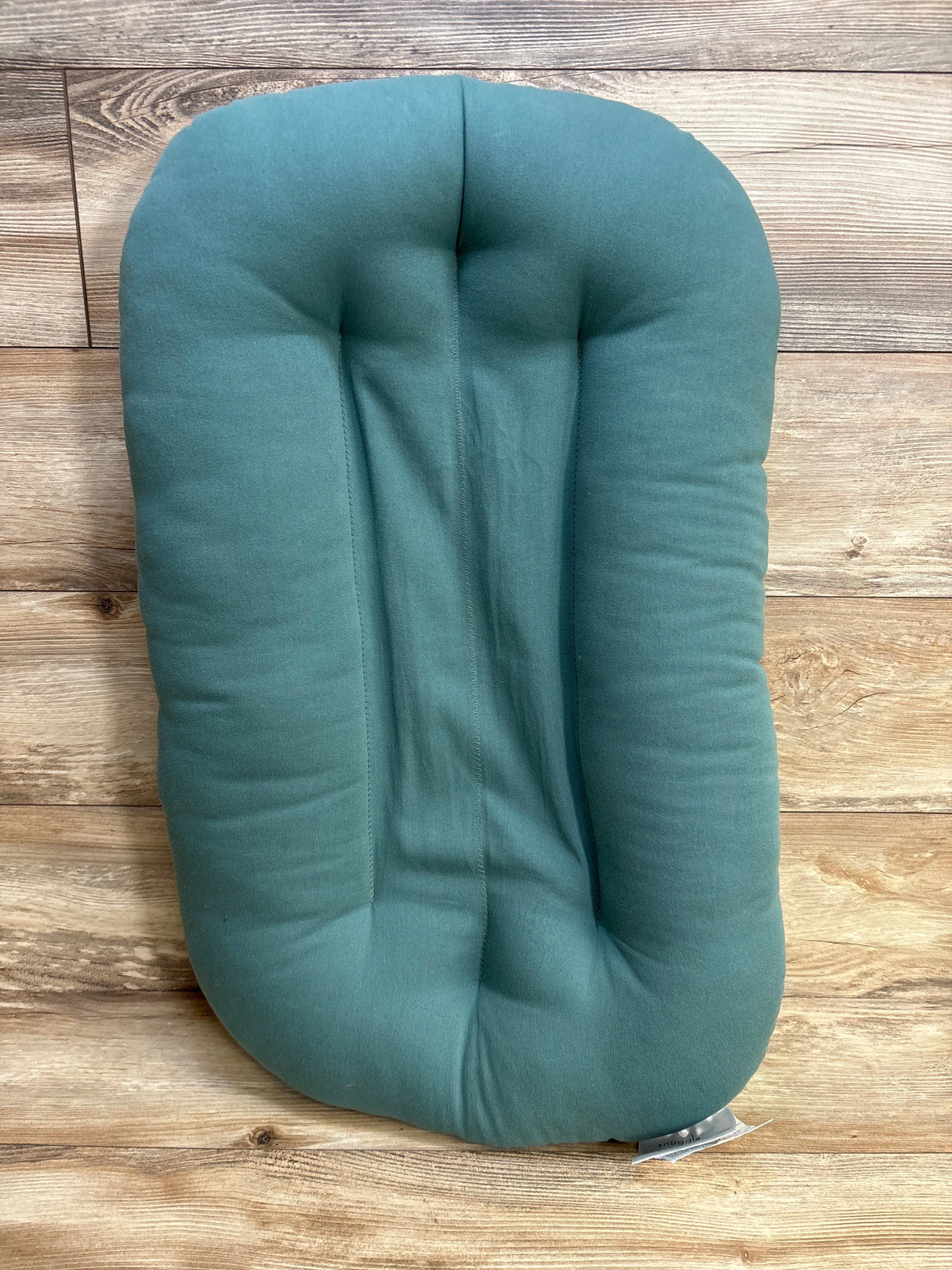 Green baby lounger pillow on wooden floor, rectangular with rounded edges