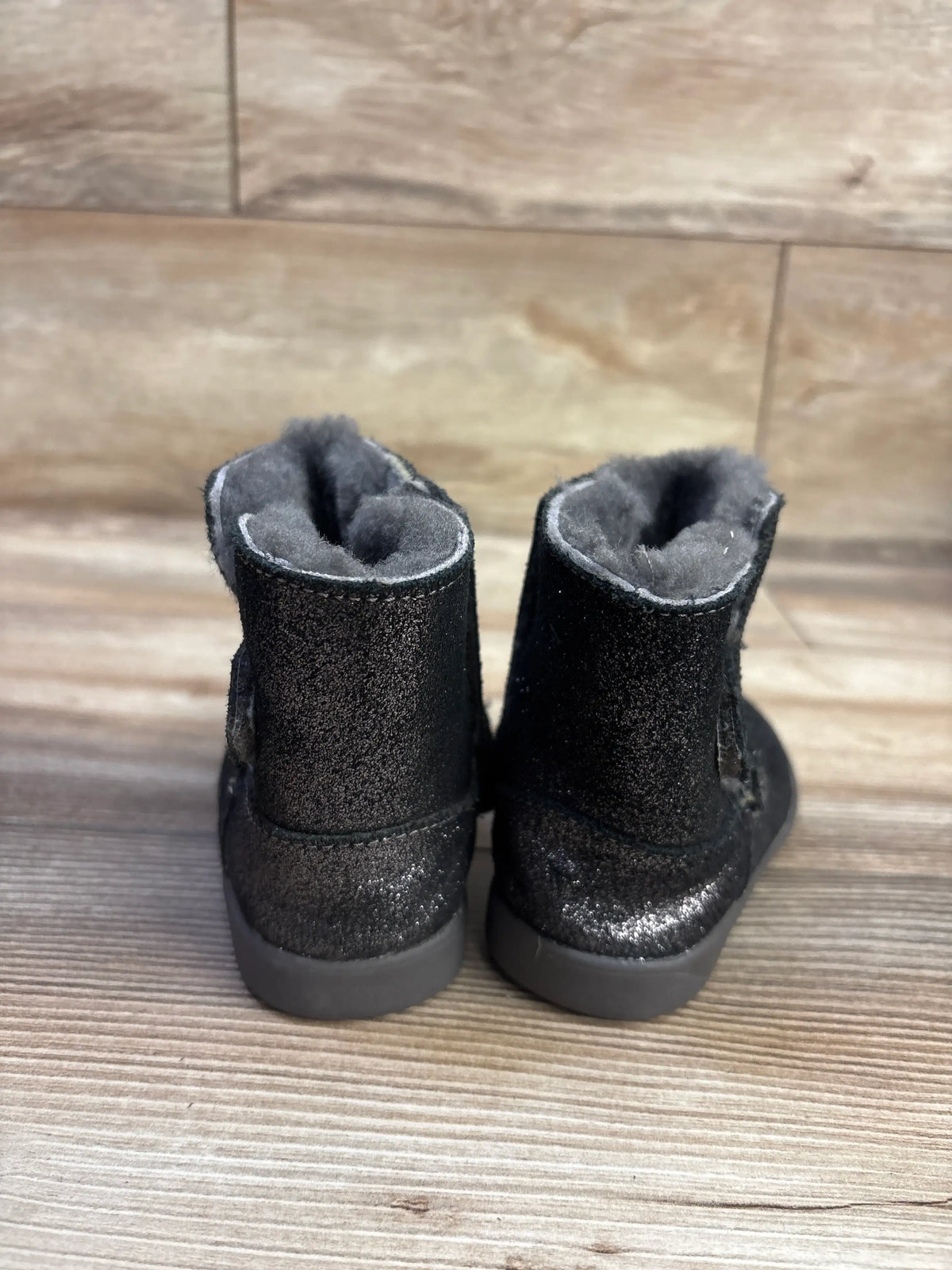 Rear view of UGG Keelan metallic glitter boots in black, size 7C, showcasing fuzzy lining on a wood background