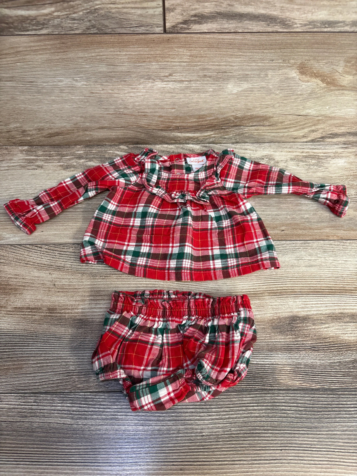 Red plaid baby outfit with ruffle long-sleeve top and matching bloomers on wood floor