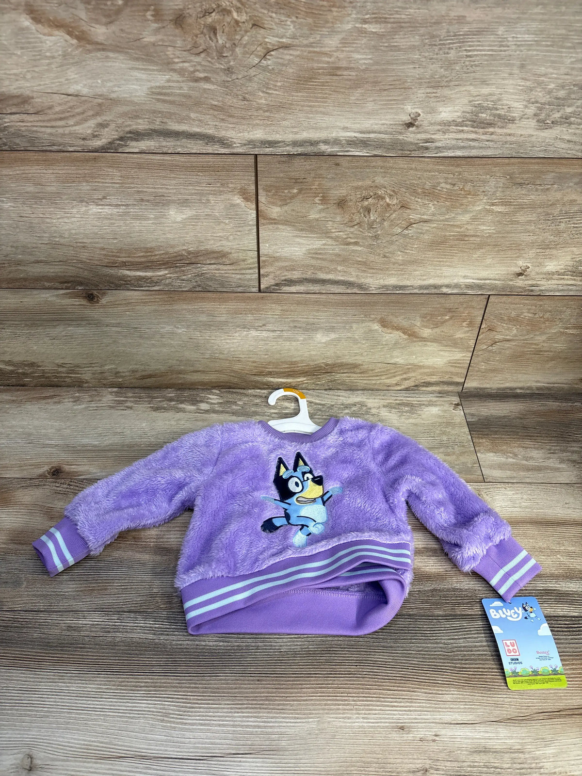 Front view of purple Bluey plush sweatshirt showcasing plush fabric, Bluey graphic, and relaxed fit on a wooden floor