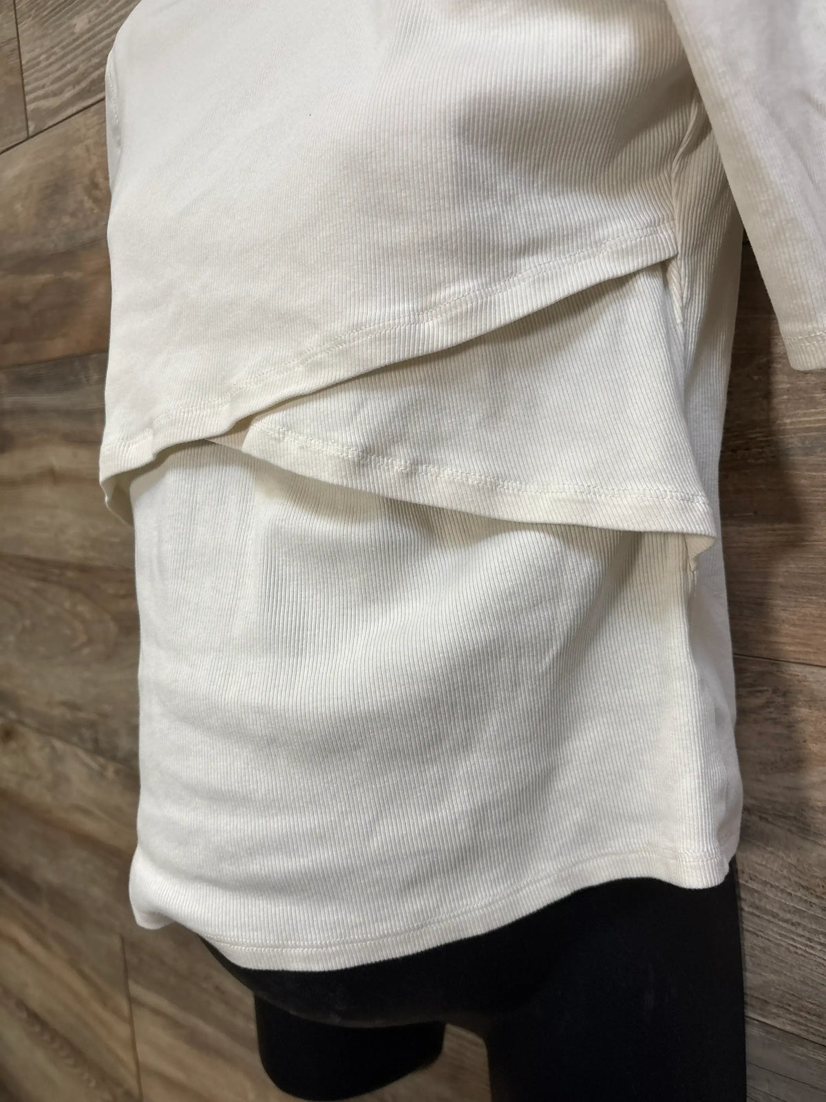Side view of H&M Mama ivory ribbed nursing shirt showing overlapping nursing flap and ribbed fabric on a mannequin against wood background