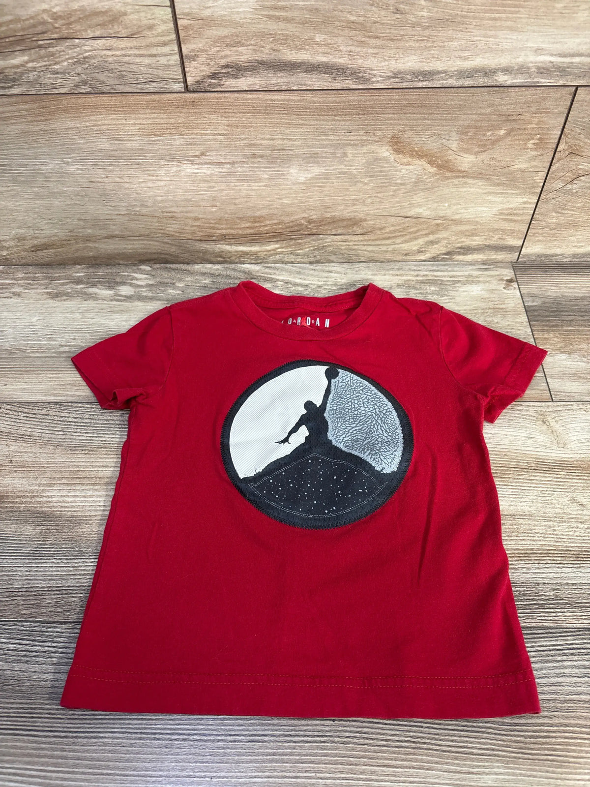 Front view of Jordan Jumpman logo shirt showcasing red short sleeves and chest graphic on a wood floor