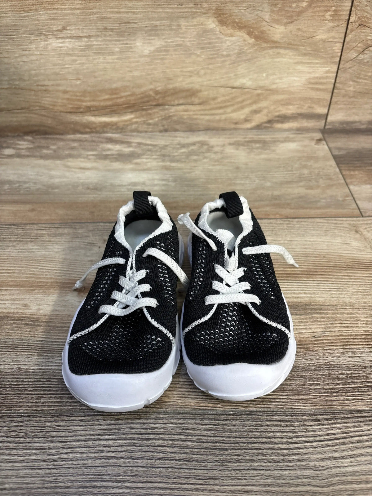 Front view of Eqw slip-on sneakers in black, size 7C, showcasing textured uppers and white soles on a wood-look floor