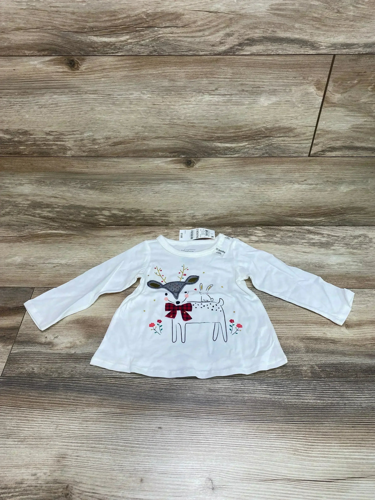 Front view of First Impressions deer shirt showcasing white long sleeve top with deer and bow graphic on wood plank floor
