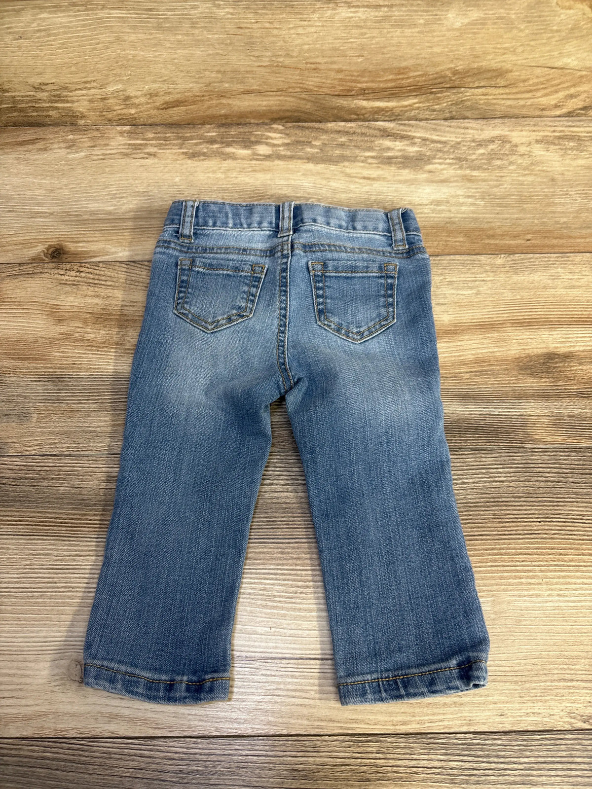 Back view of Cat & Jack skinny distressed sequin jeans in blue showcasing stitched back pockets on a wood-grain background
