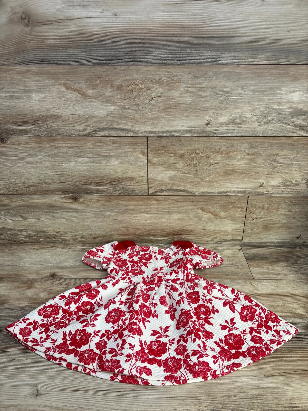 Flat lay of Janie & Jack 2T toddler dress showing quilted maroon floral print, puff sleeves and front bow on wood surface