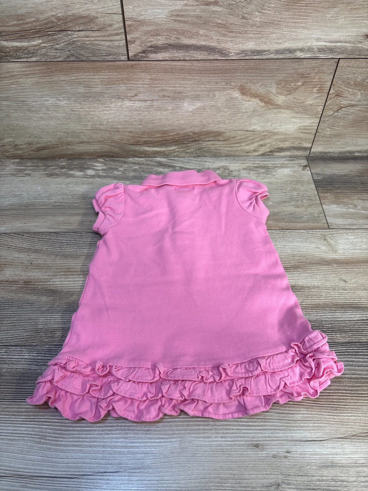 Pink baby dress with ruffled hem and short sleeves on wood background