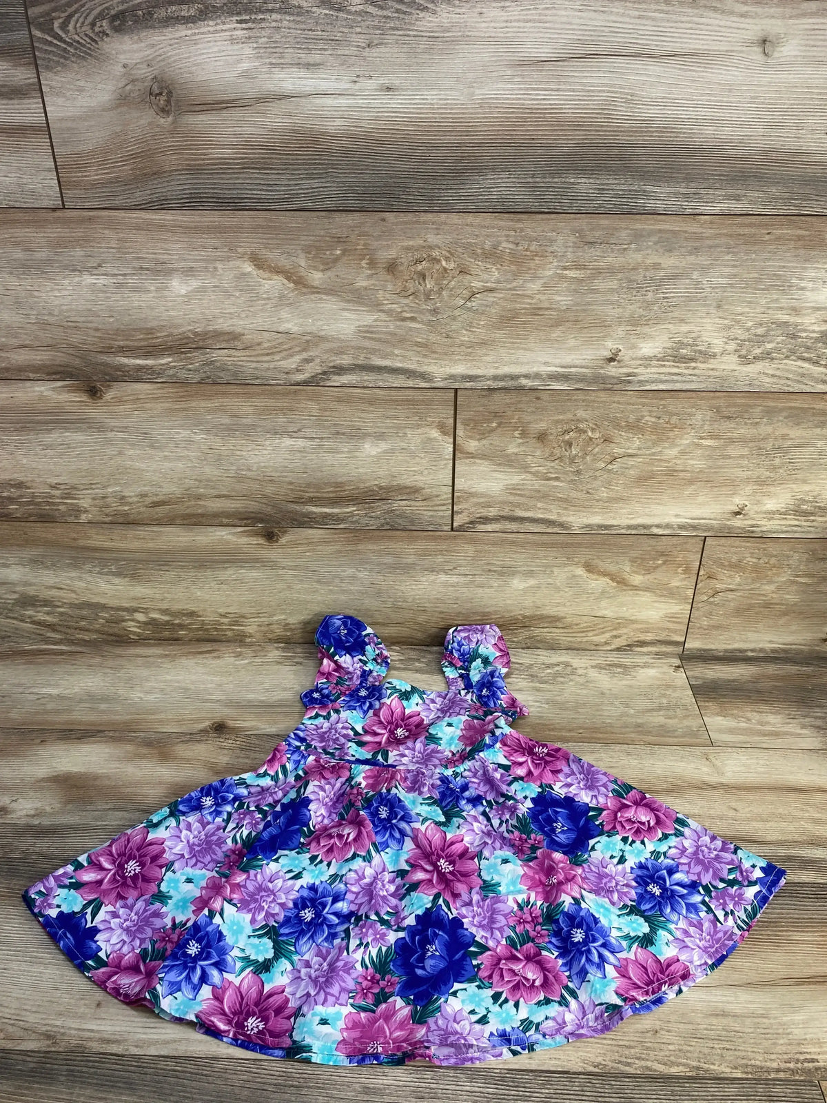 Flat lay of Janie and Jack floral dress with blue purple and pink flower print and shoulder ties on wood plank floor