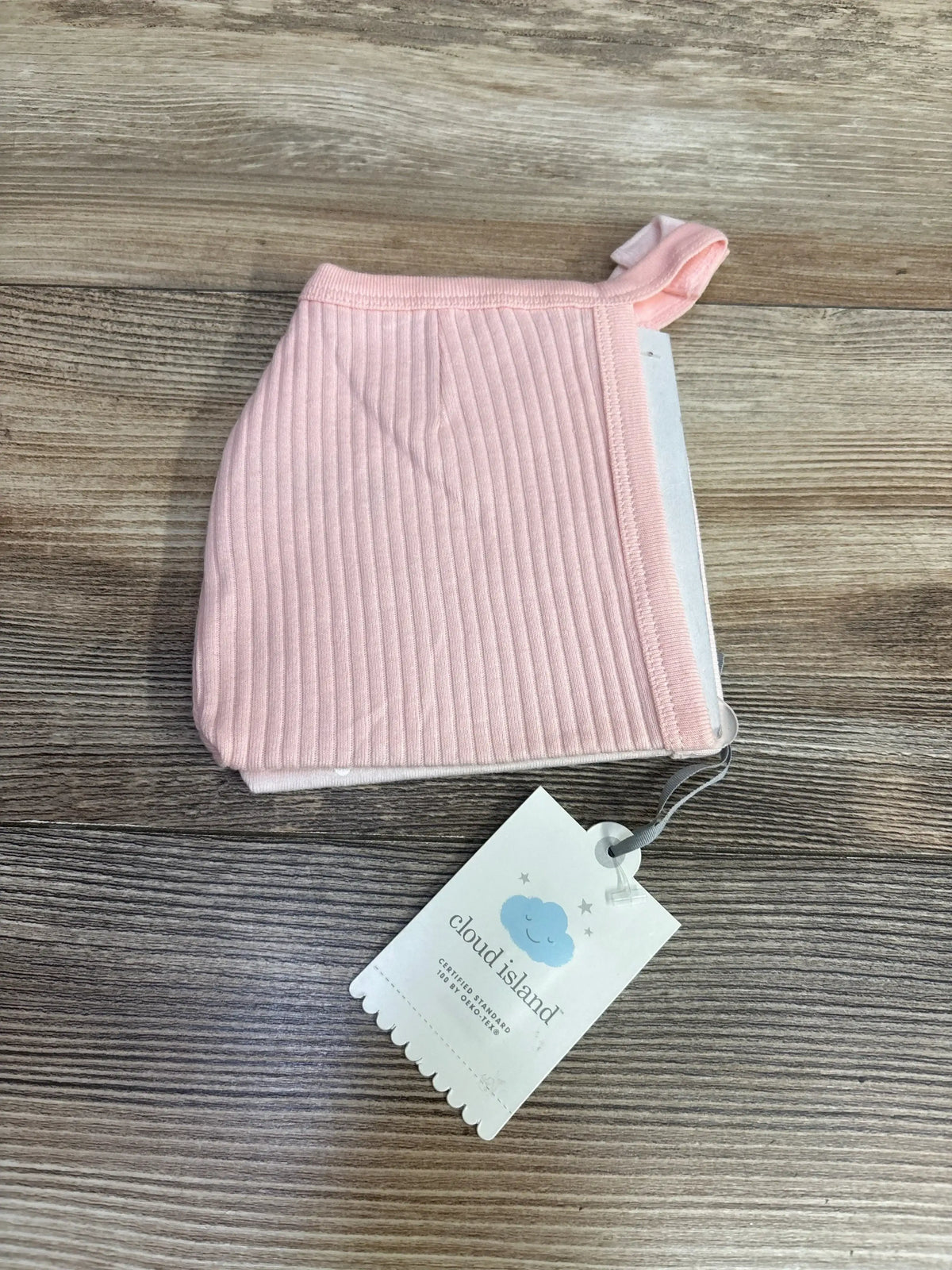 Top-down view of Cloud Island newborn pink ribbed cotton bonnet showcasing ribbed texture and attached brand tag on wood surface