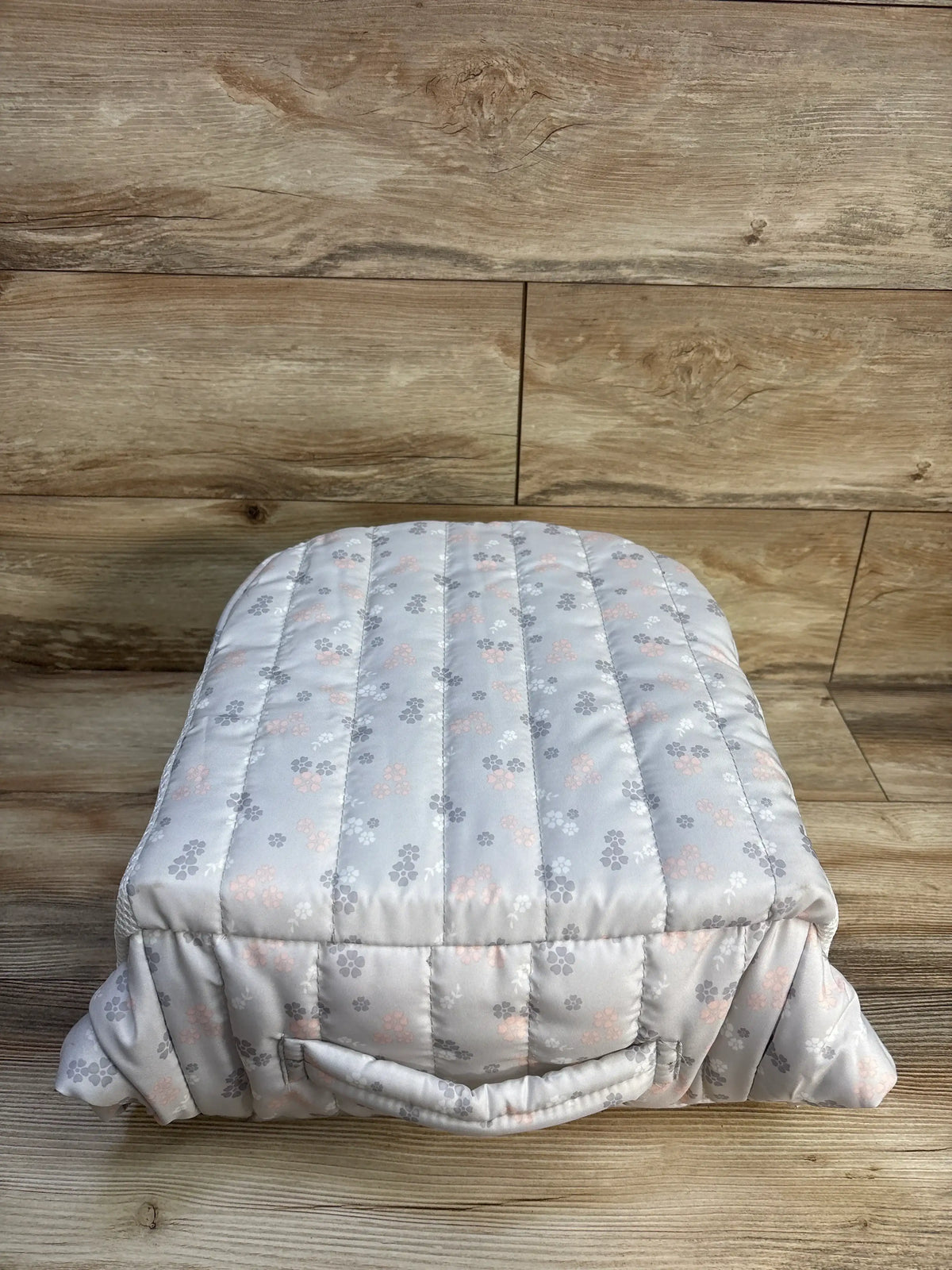 Front view of Baby Delight Snuggle Nest Harmony Portable Infant Lounger showcasing its light gray quilted cover with pink and gray floral pattern on a wood floor
