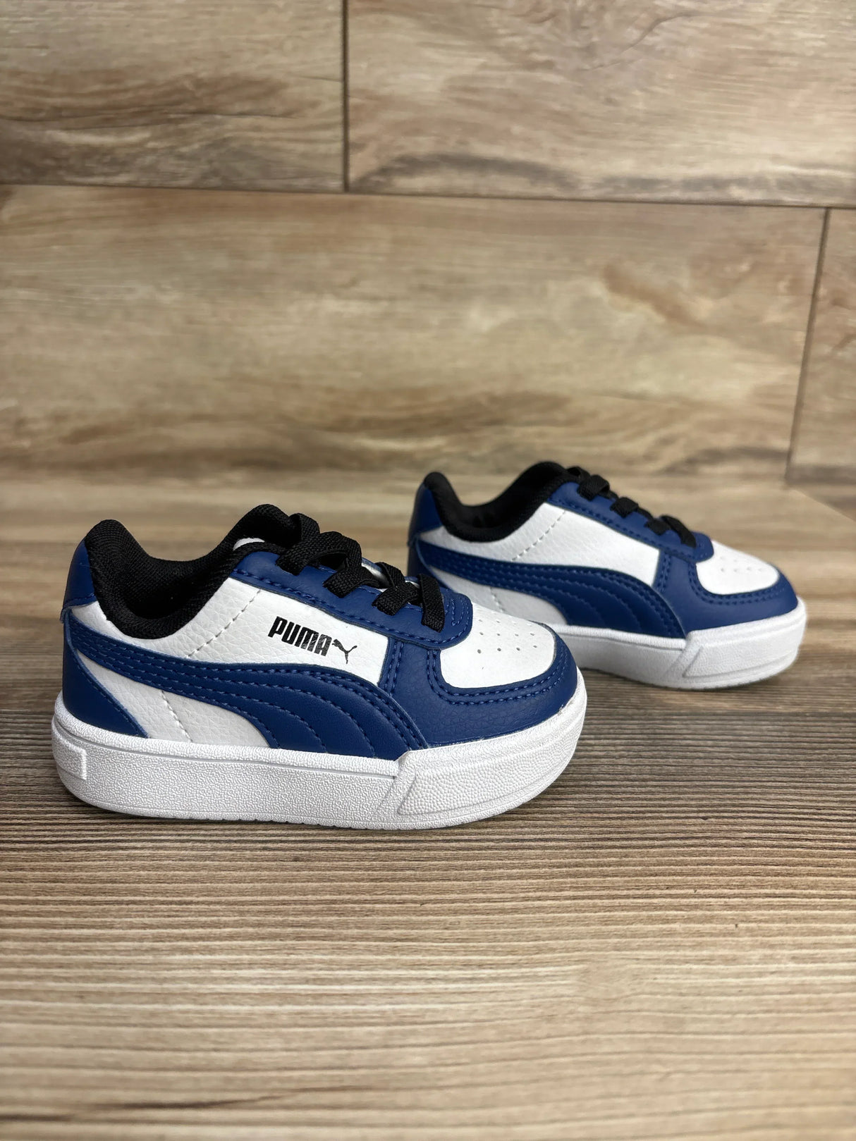 Blue and white Puma toddler sneakers with black laces on a wood background