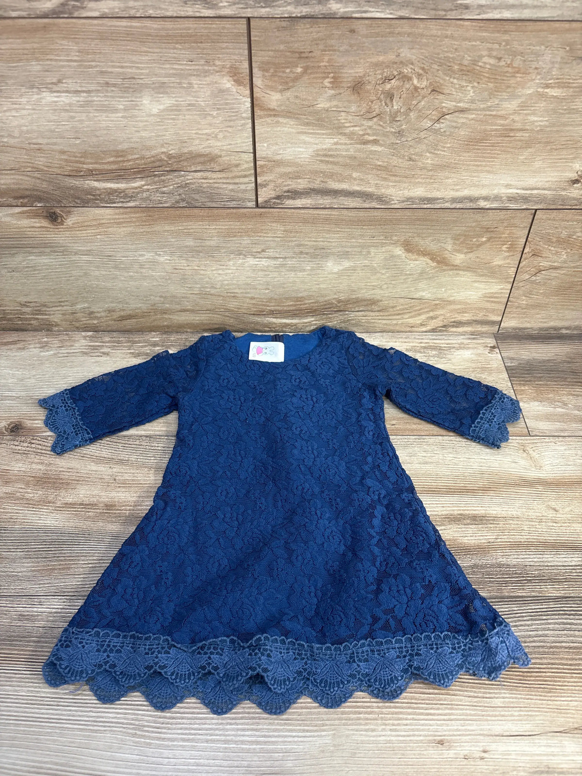 Front view of blue long sleeve lace dress, size 18 to 24 months, showcasing scalloped lace trim on a wood floor