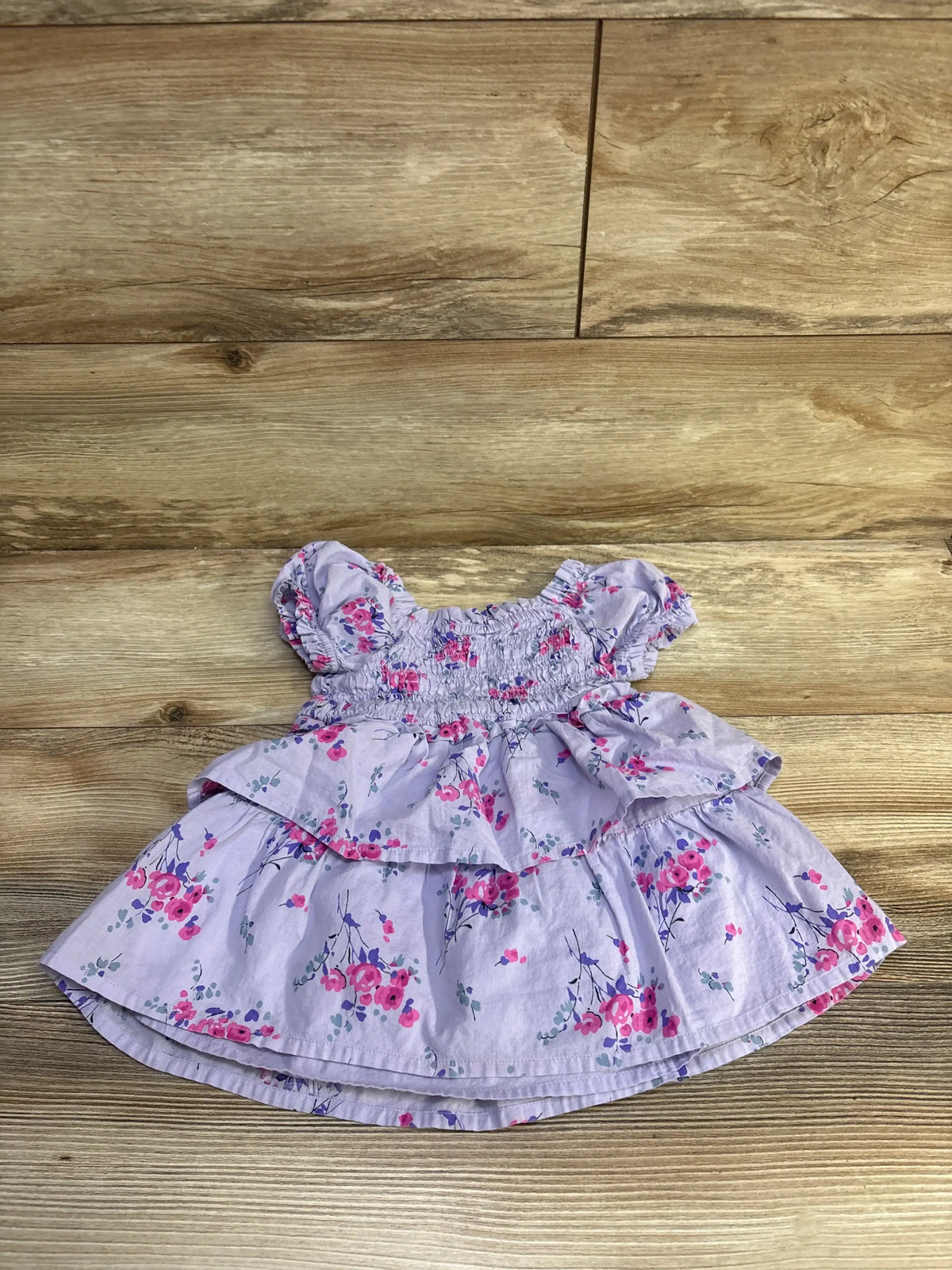 Flat lay of purple Baby Gap smocked puff-sleeve baby dress with tiered floral skirt on wood background