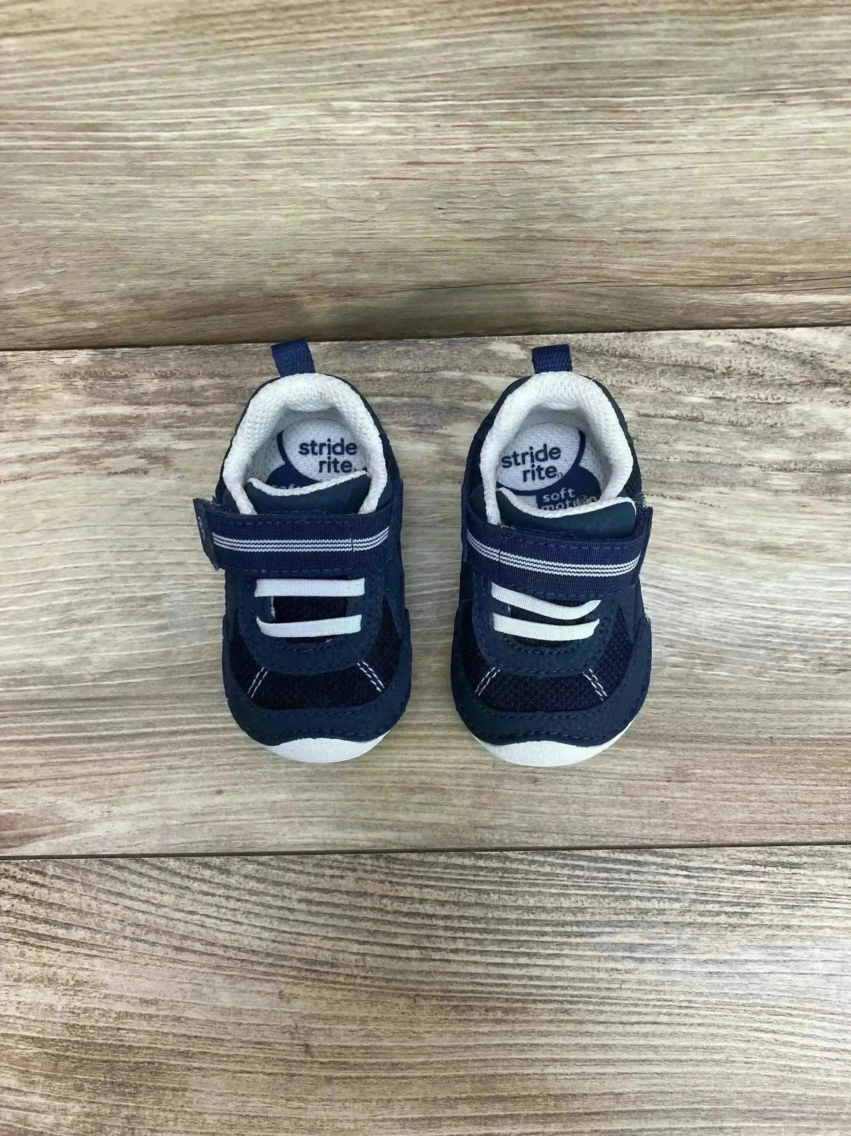 Top view of navy and white Stride Rite toddler sneakers showing Velcro strap, breathable mesh panels, and white toe cap on light wood floor