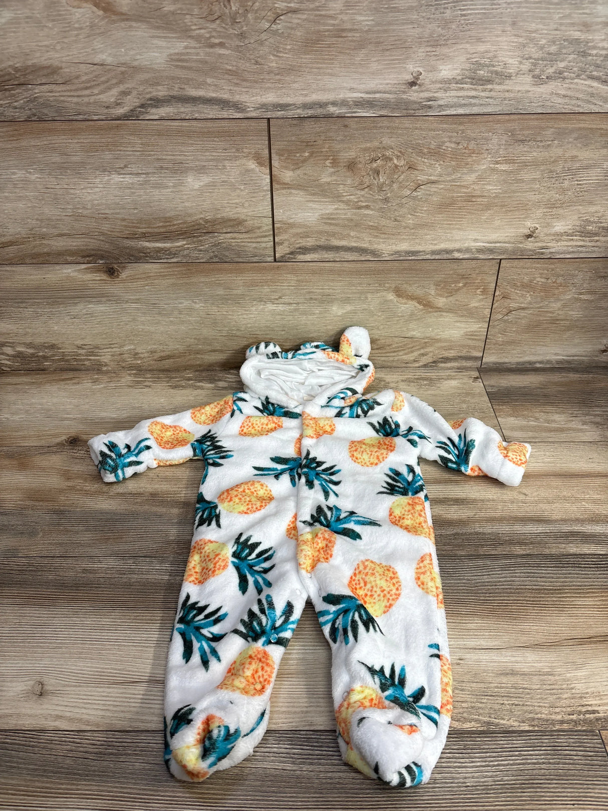 White fleece baby sleeper with pineapple print and hood, displayed on wood floor