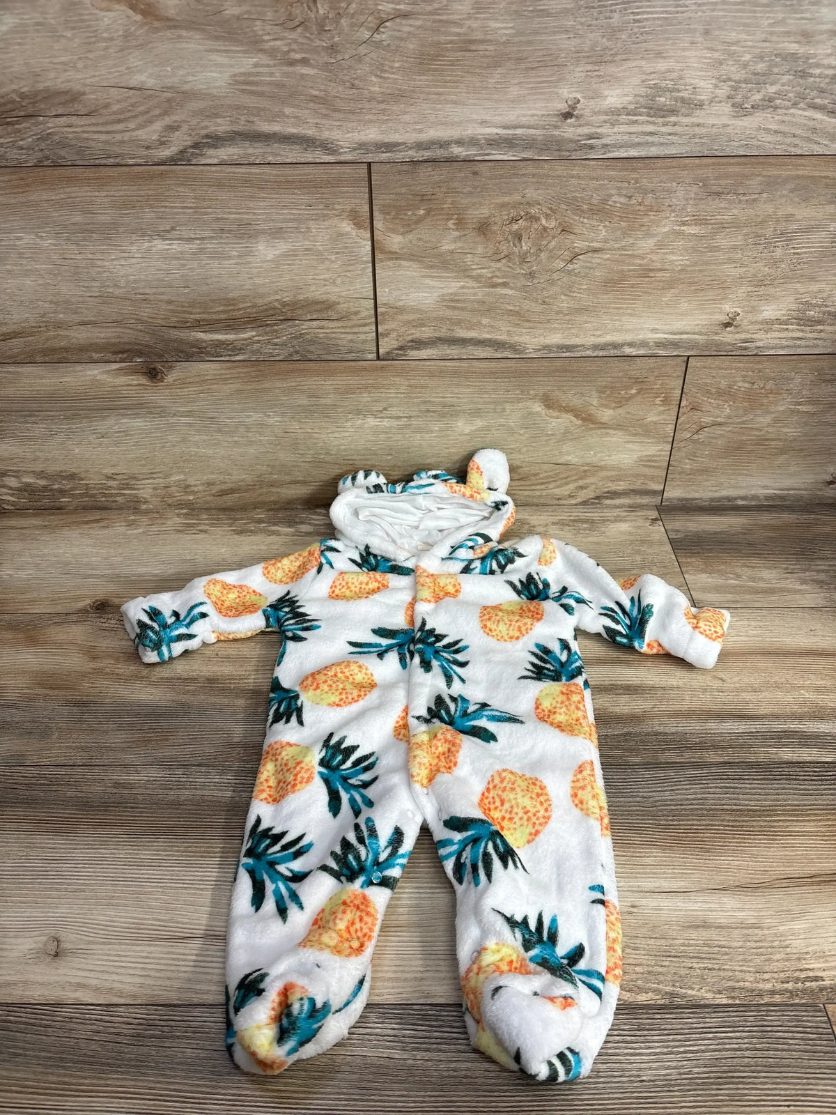 White fleece baby sleeper with pineapple print and hood, displayed on wood floor
