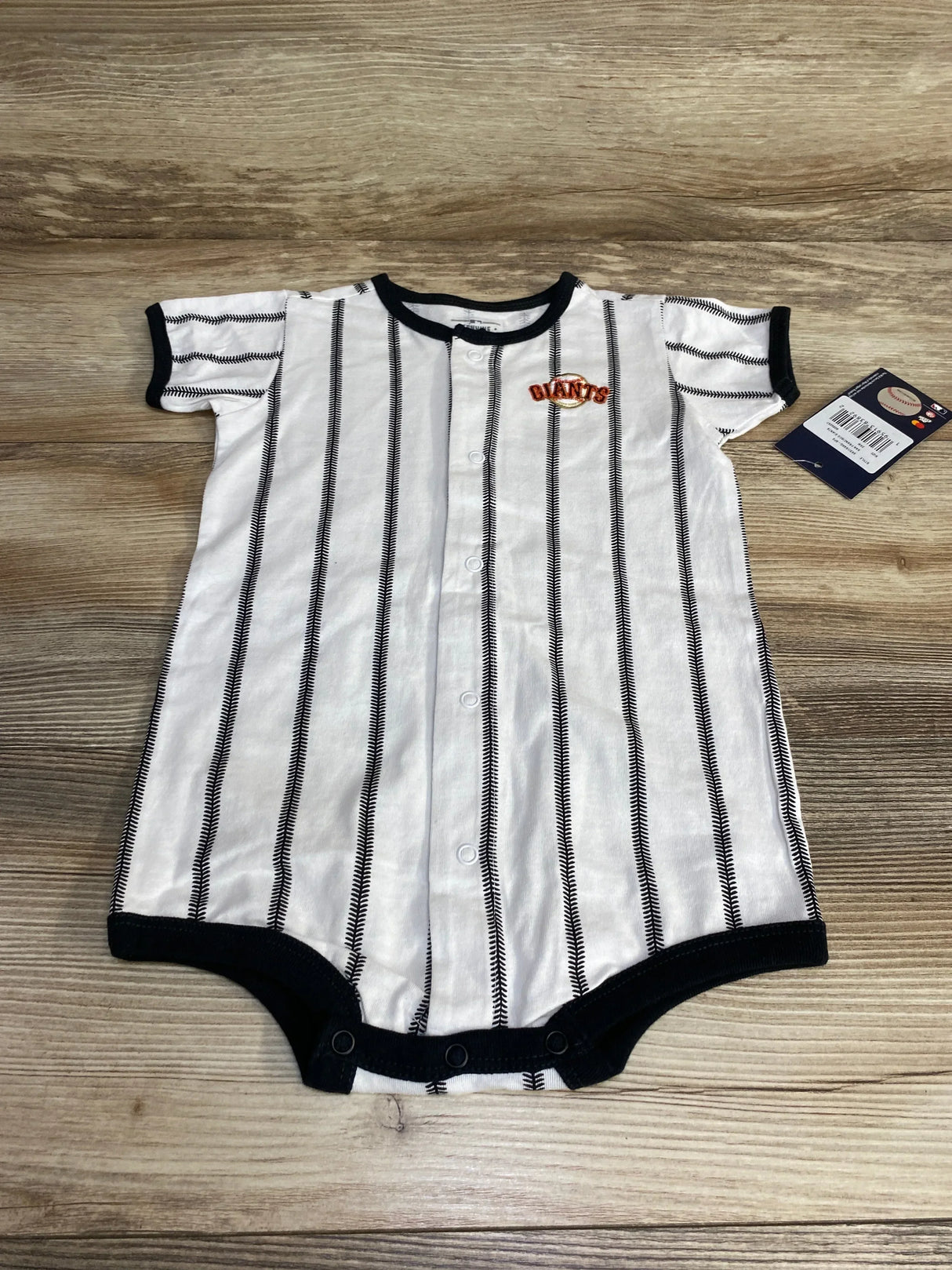 Flat lay of white San Francisco Giants pinstripe romper (24M) showing front snaps, black trim and chest Giants patch on wood background