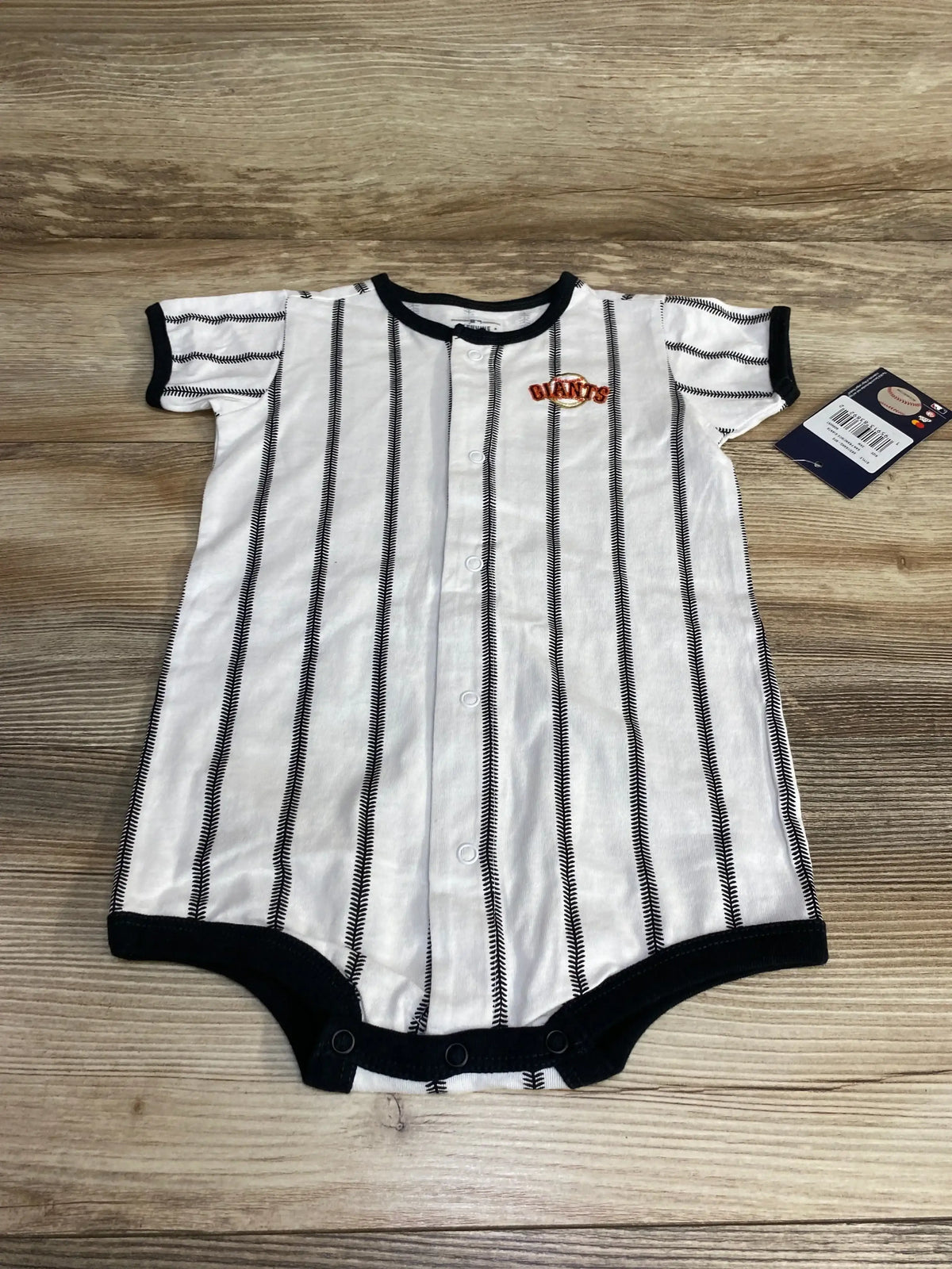Flat lay of white San Francisco Giants pinstripe romper (24M) showing front snaps, black trim and chest Giants patch on wood background