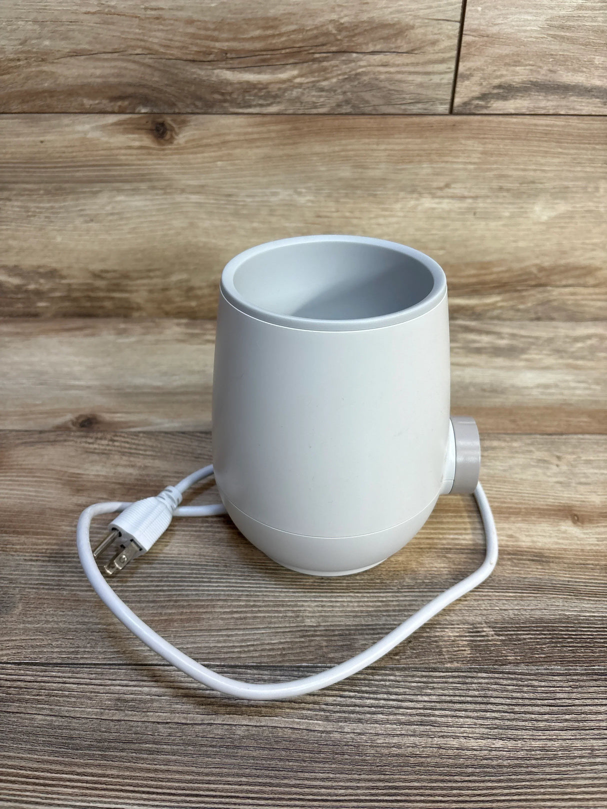 White electric baby bottle warmer on wooden surface with power cord