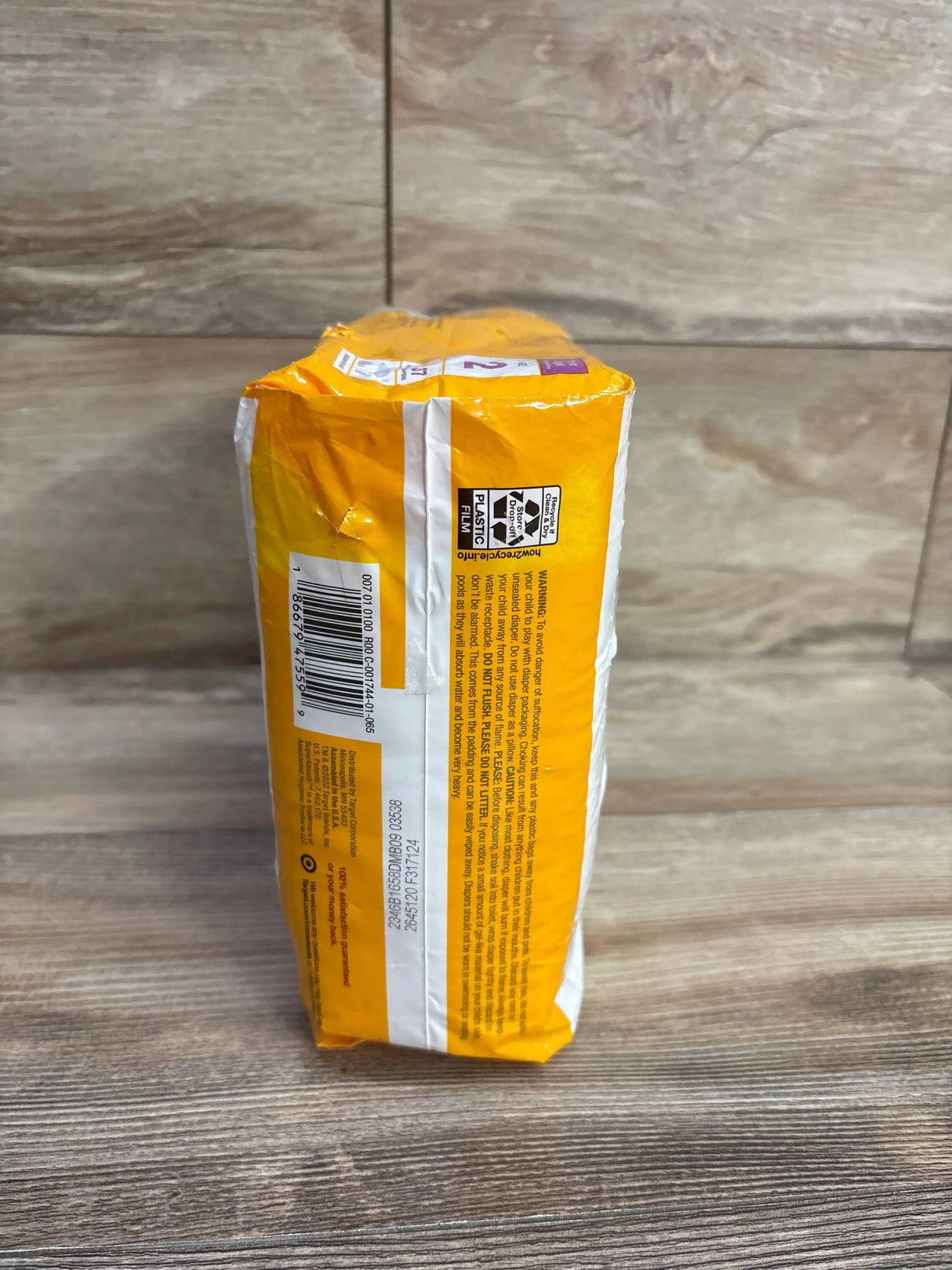 Packaged yellow baby diapers with barcode and recycling info on wooden surface