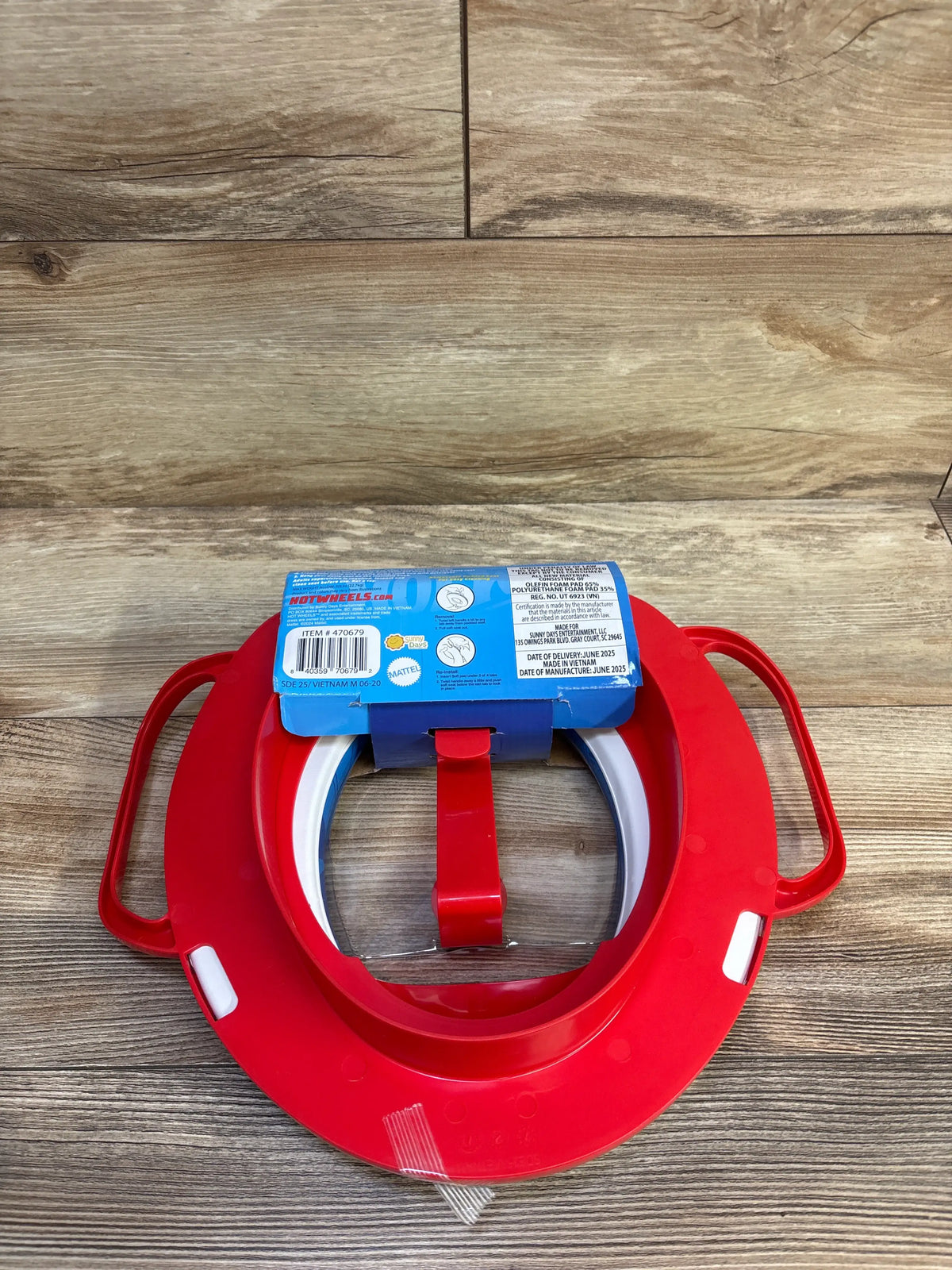 Top view of red Hot Wheels soft potty training seat with side handles and white inserts on a wood-look floor