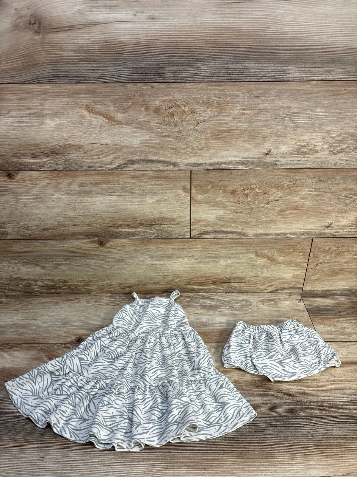 Top view of Makemake Organics white sleeveless dress and bloomers set showcasing gray leaf pattern with wooden background
