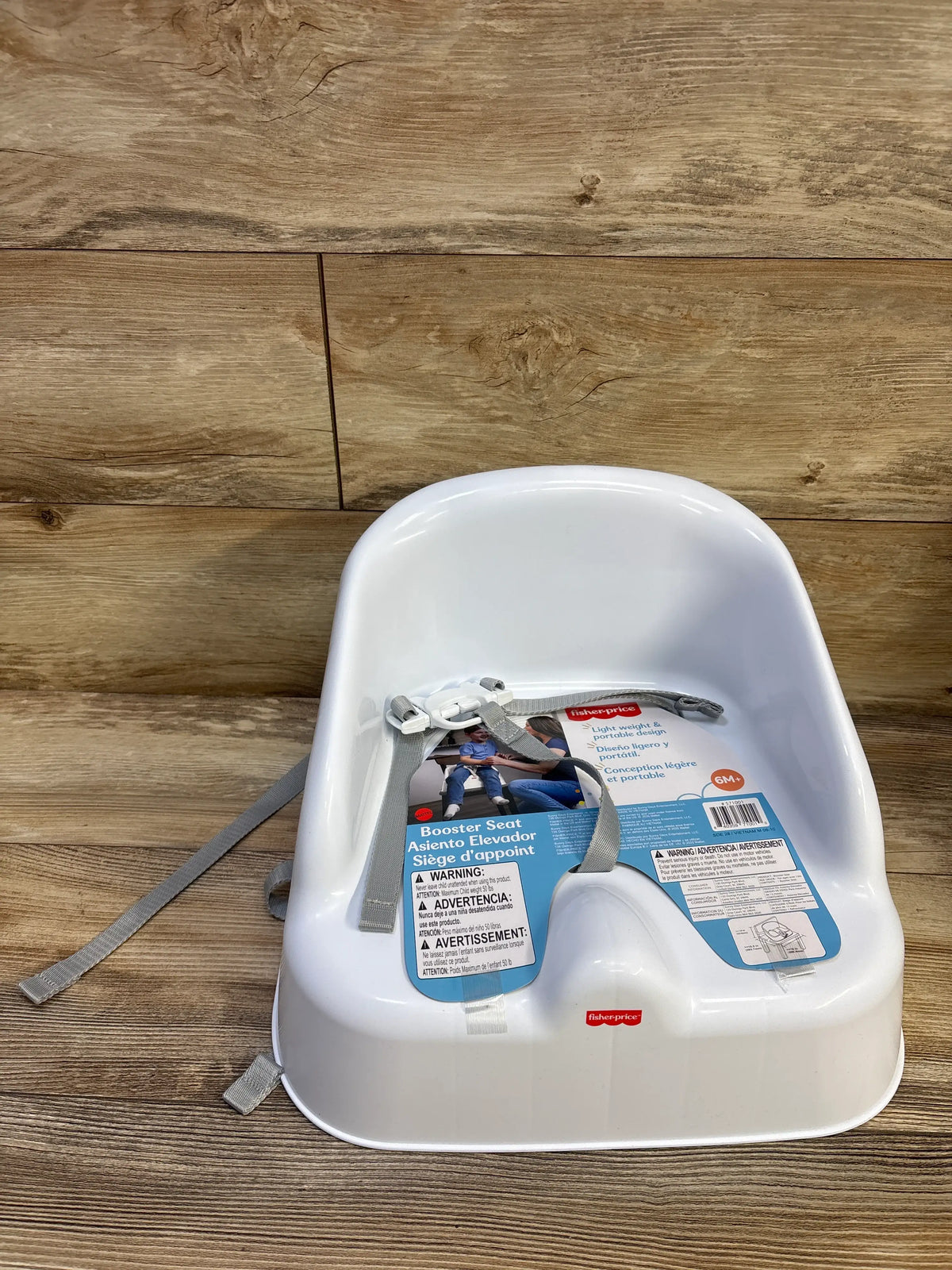 Front view of a white Fisher-Price booster seat showcasing gray safety straps and portable design on a wood floor