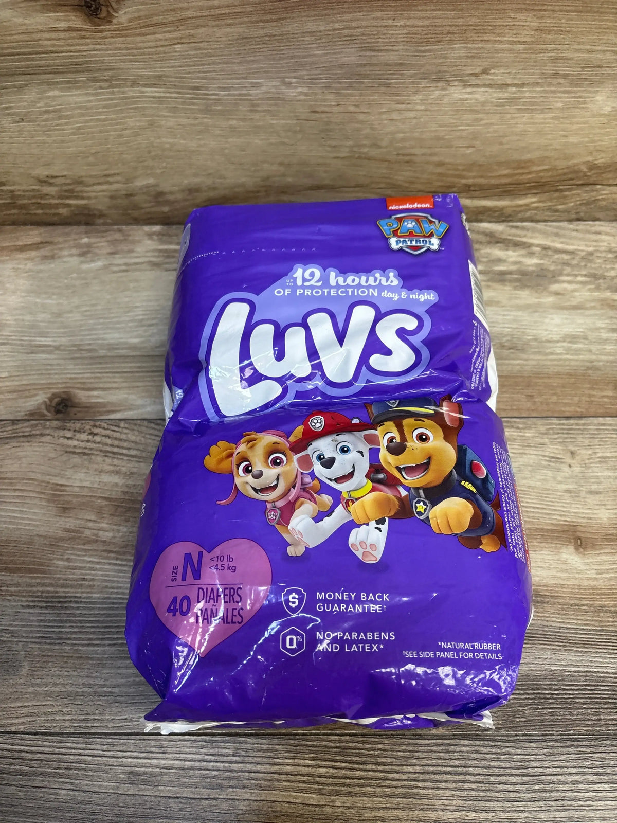 Top-down view of Luvs newborn 40-count diaper pack showing Paw Patrol characters and '12 hours' protection claim on purple packaging